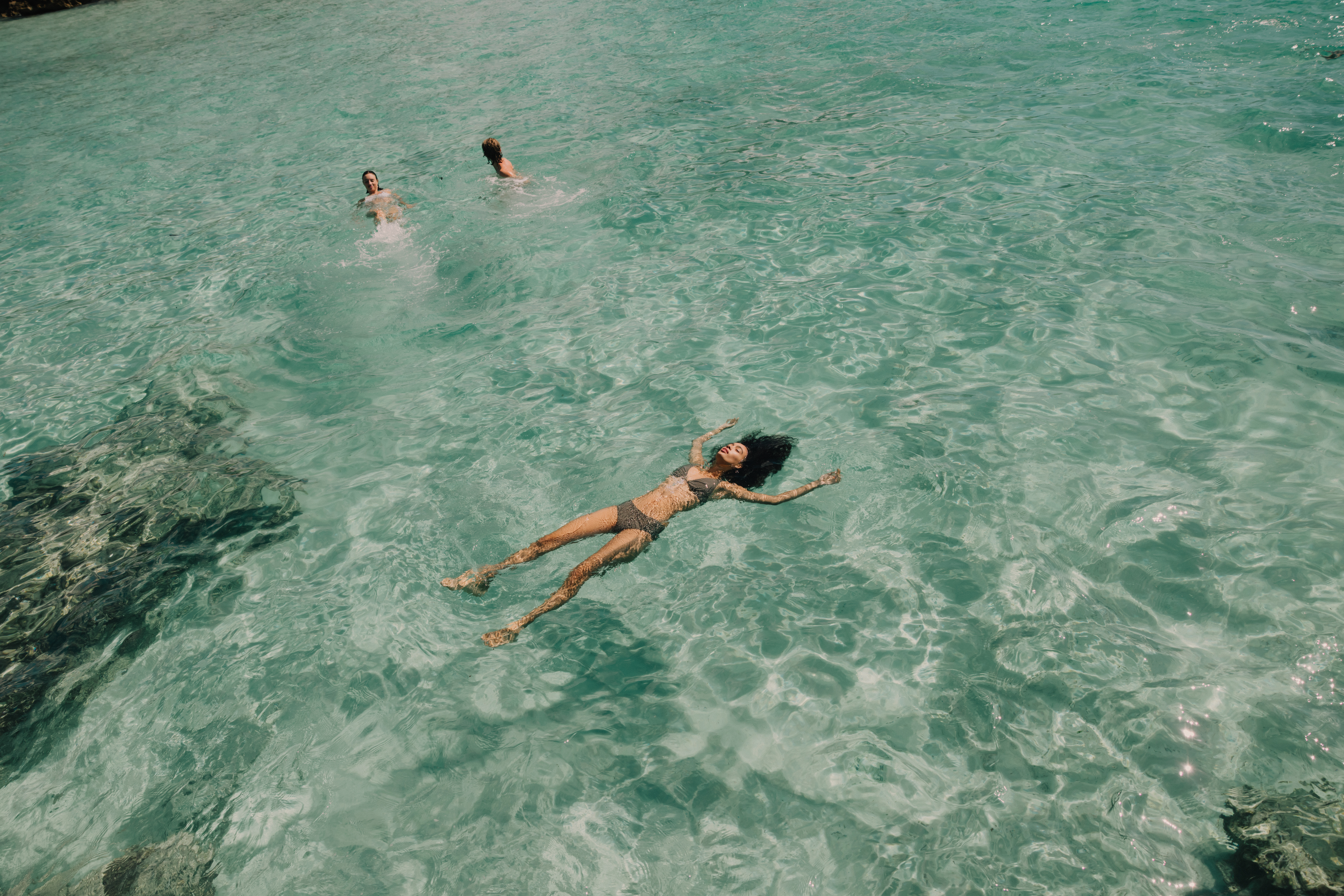 Woman in bikini floating on back in clear turquoise ocean with swimmers.
