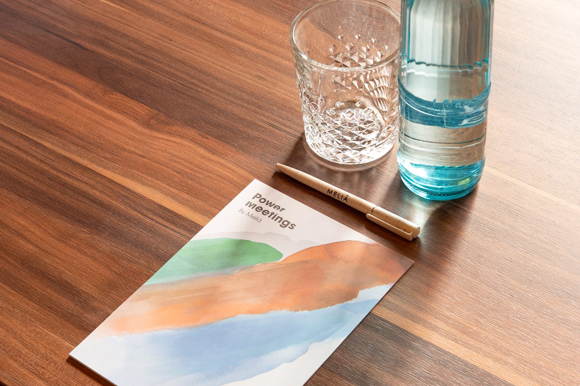 Meeting table with Meliá 'Power meetings' brochure, water bottle, glass, and pen.