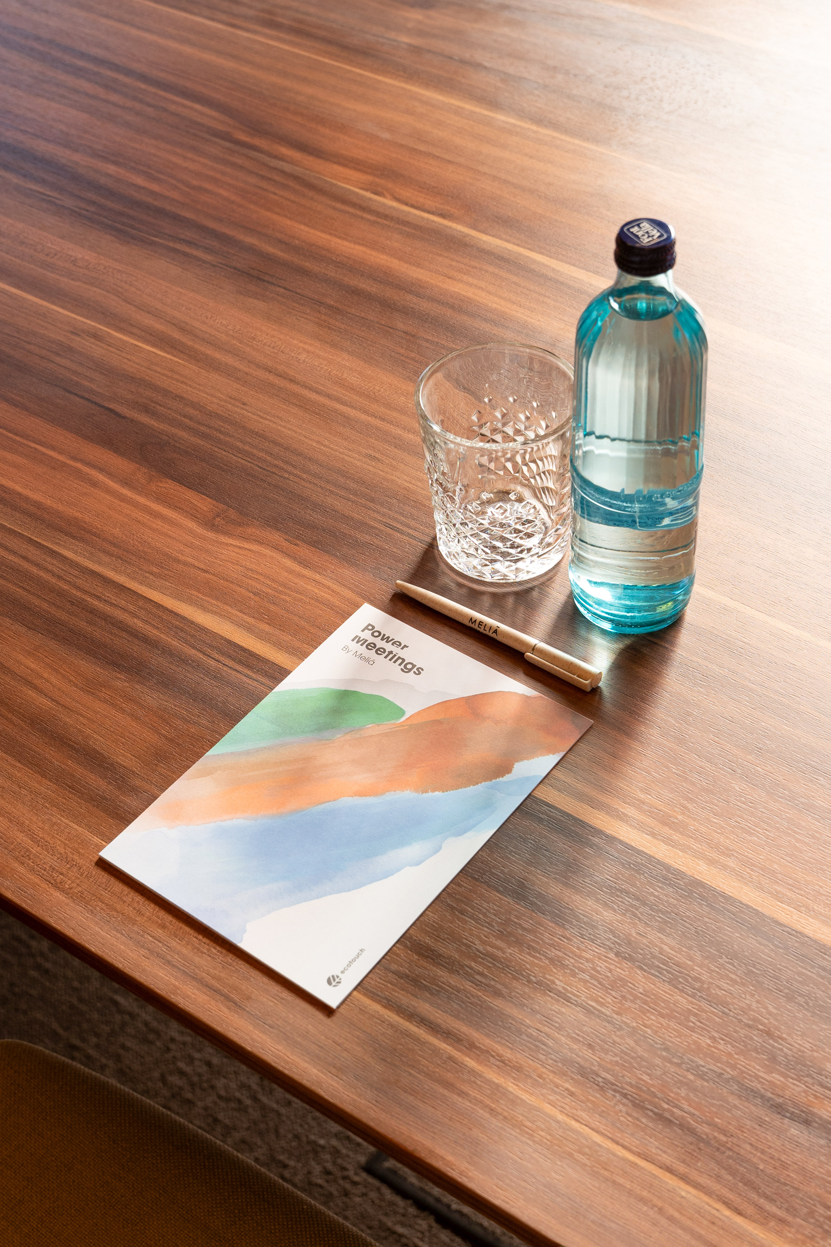 Meeting table with Meliá 'Power meetings' brochure, water bottle, glass, and pen.