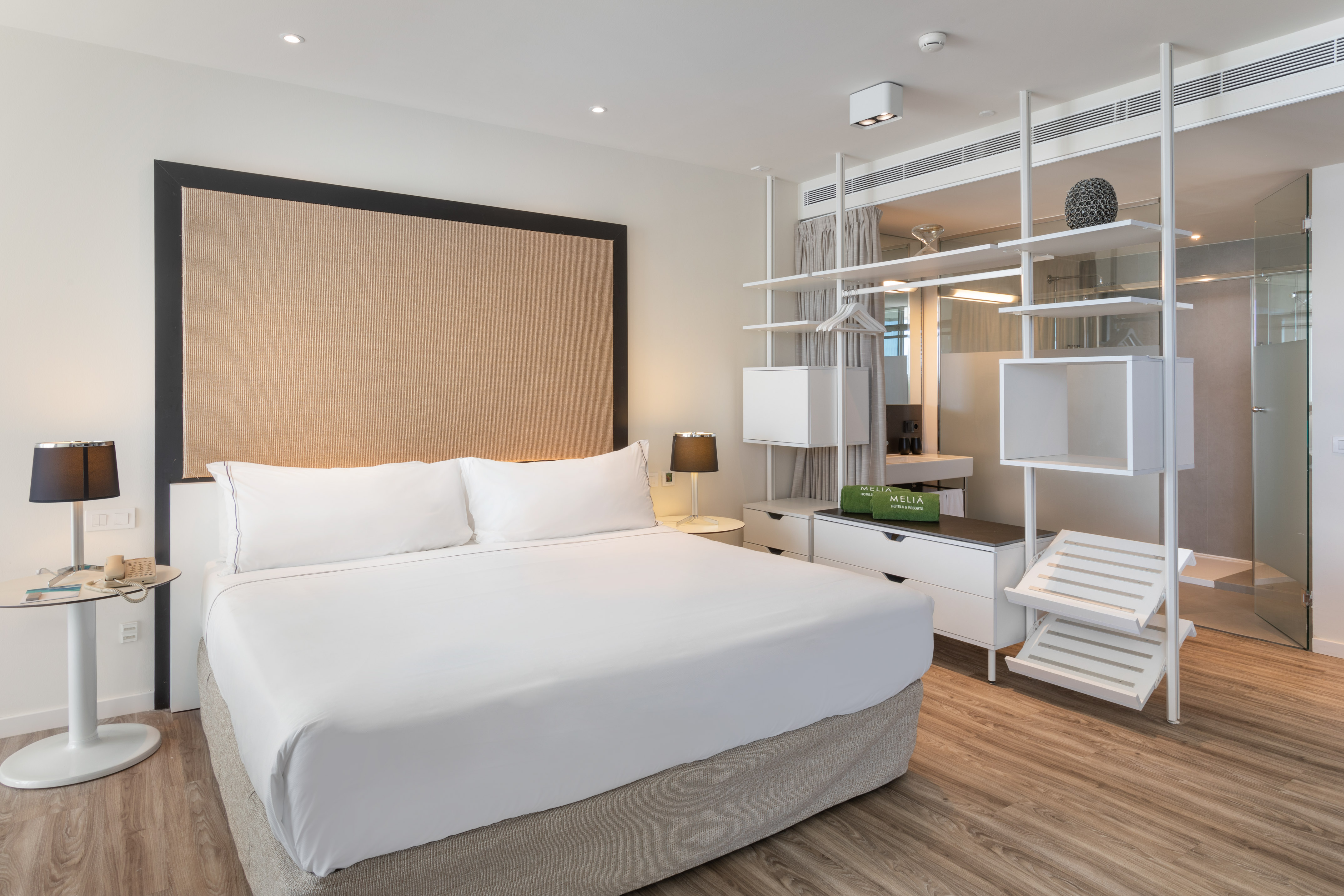 Modern hotel bedroom with king bed, white linens, and open wardrobe design.