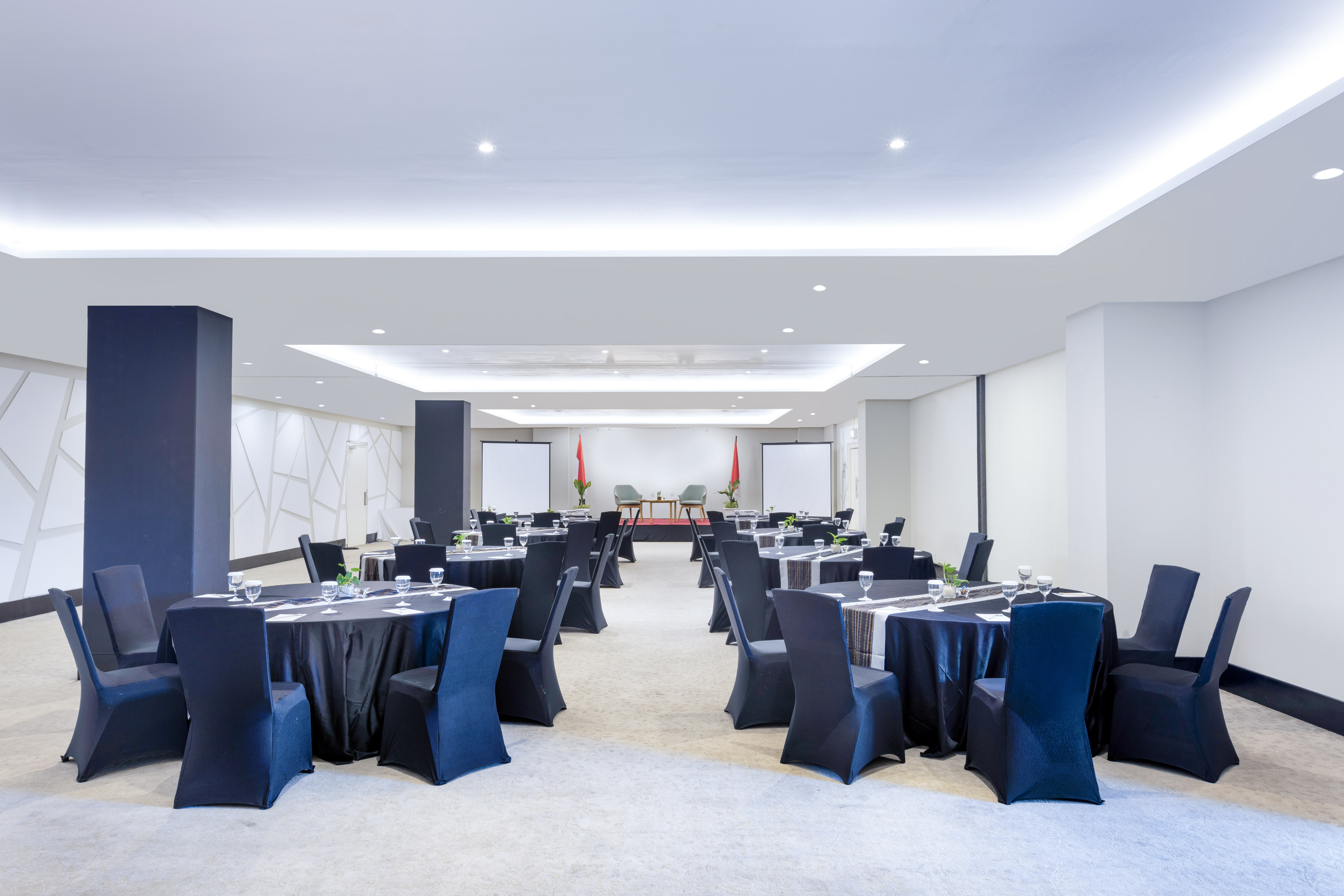 Modern conference room with round tables, black chairs, two screens, and stage.