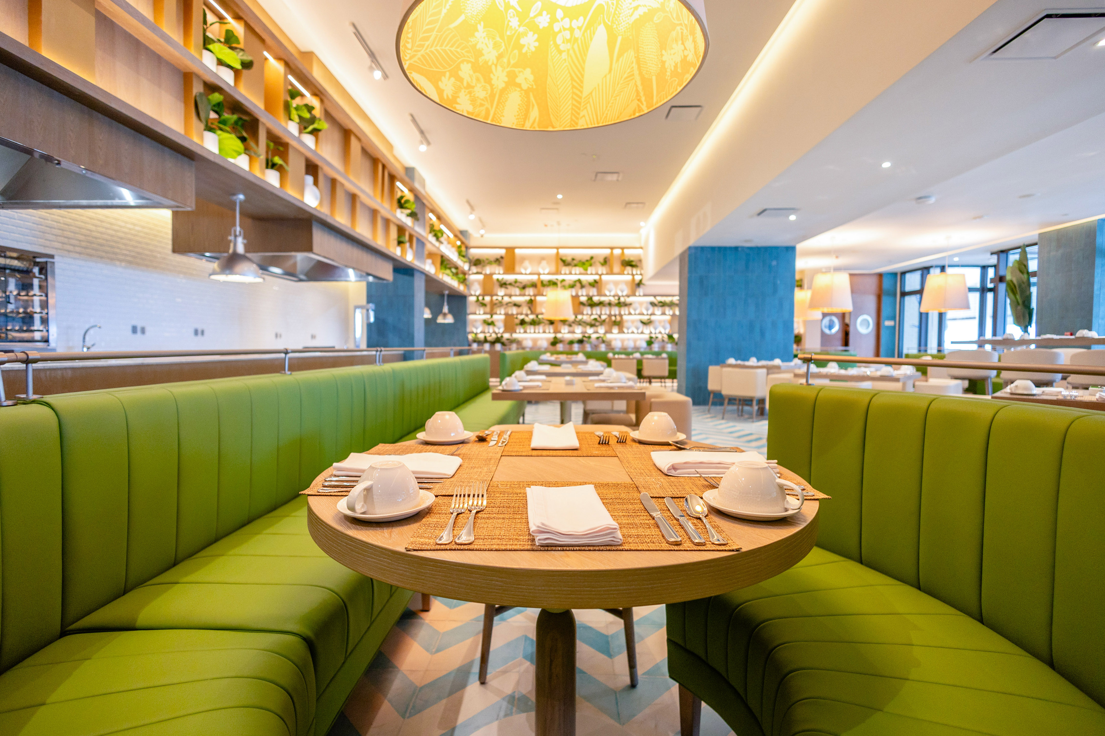 Modern restaurant with green booths, wooden tables, and illuminated plant decor.