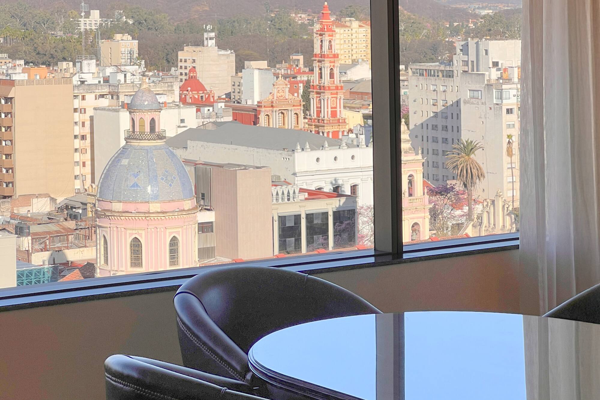 Hotel room city view: historic church domes, urban buildings, and distant mountains.