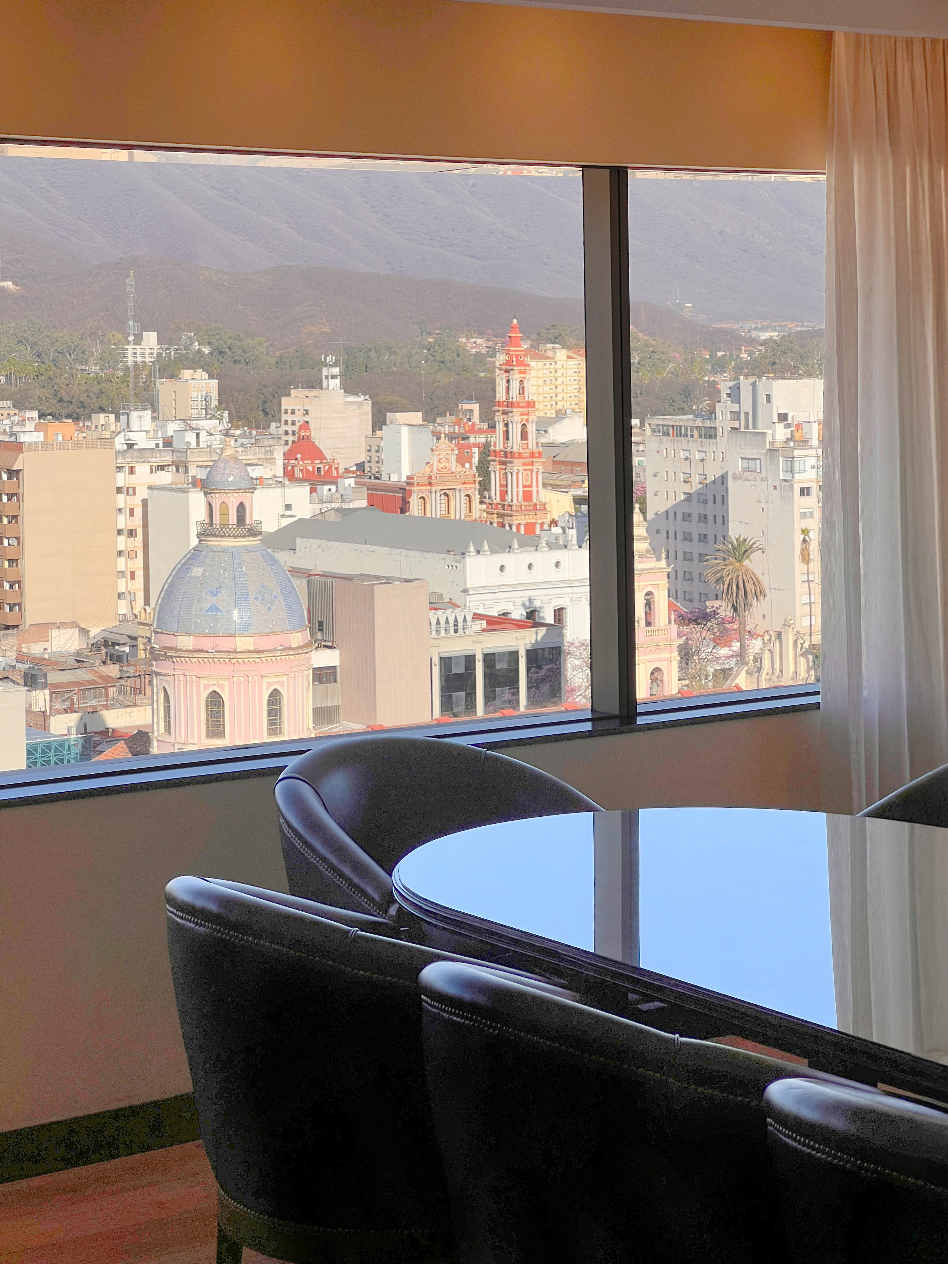 Hotel room city view: historic church domes, urban buildings, and distant mountains.