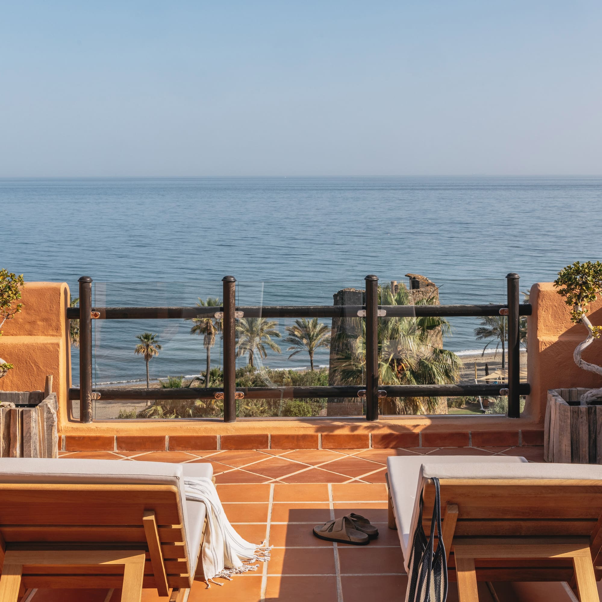 Oceanfront balcony with lounge chairs, palm trees, and beach view.