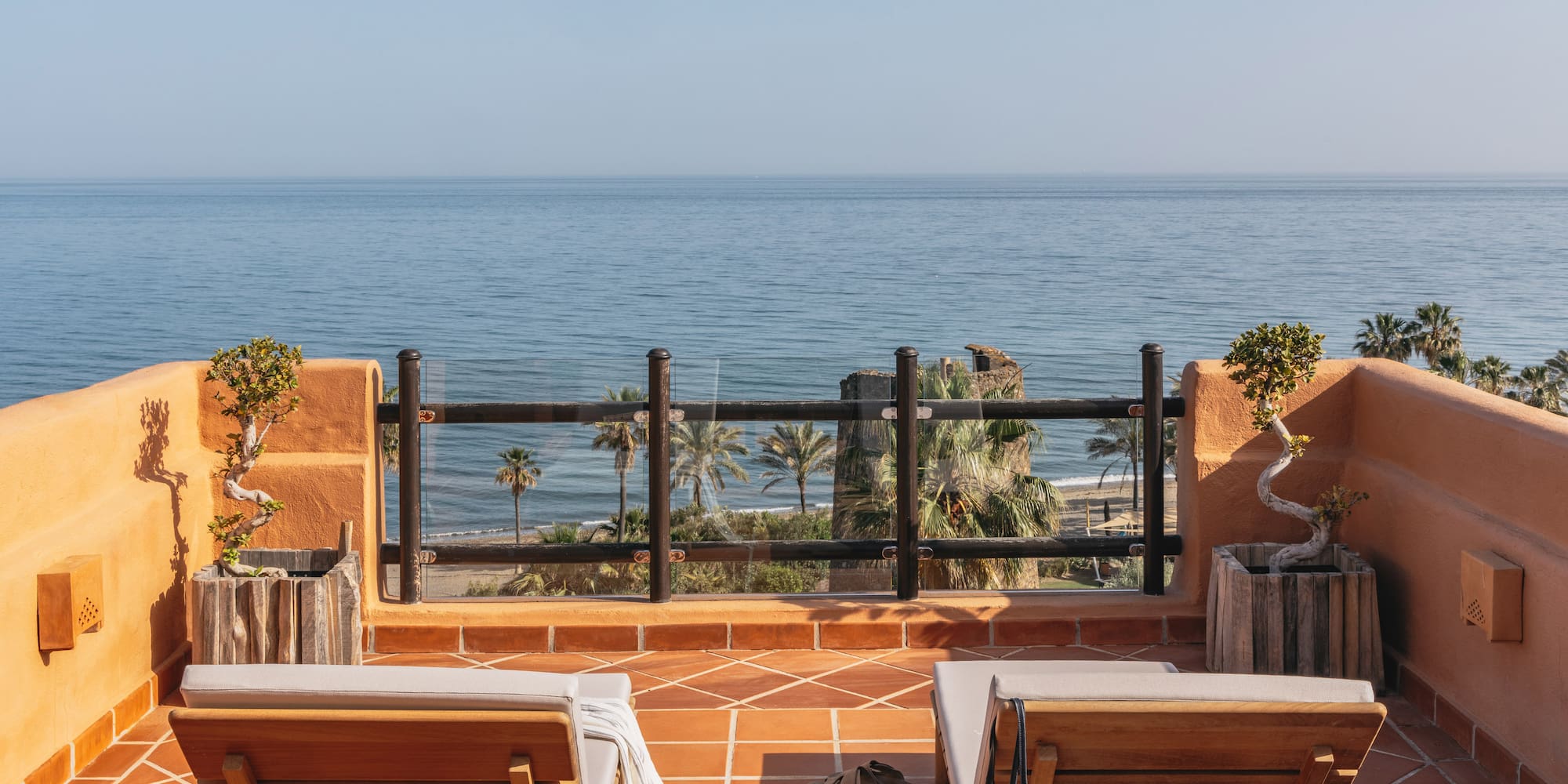 Oceanfront balcony with lounge chairs, palm trees, and beach view.