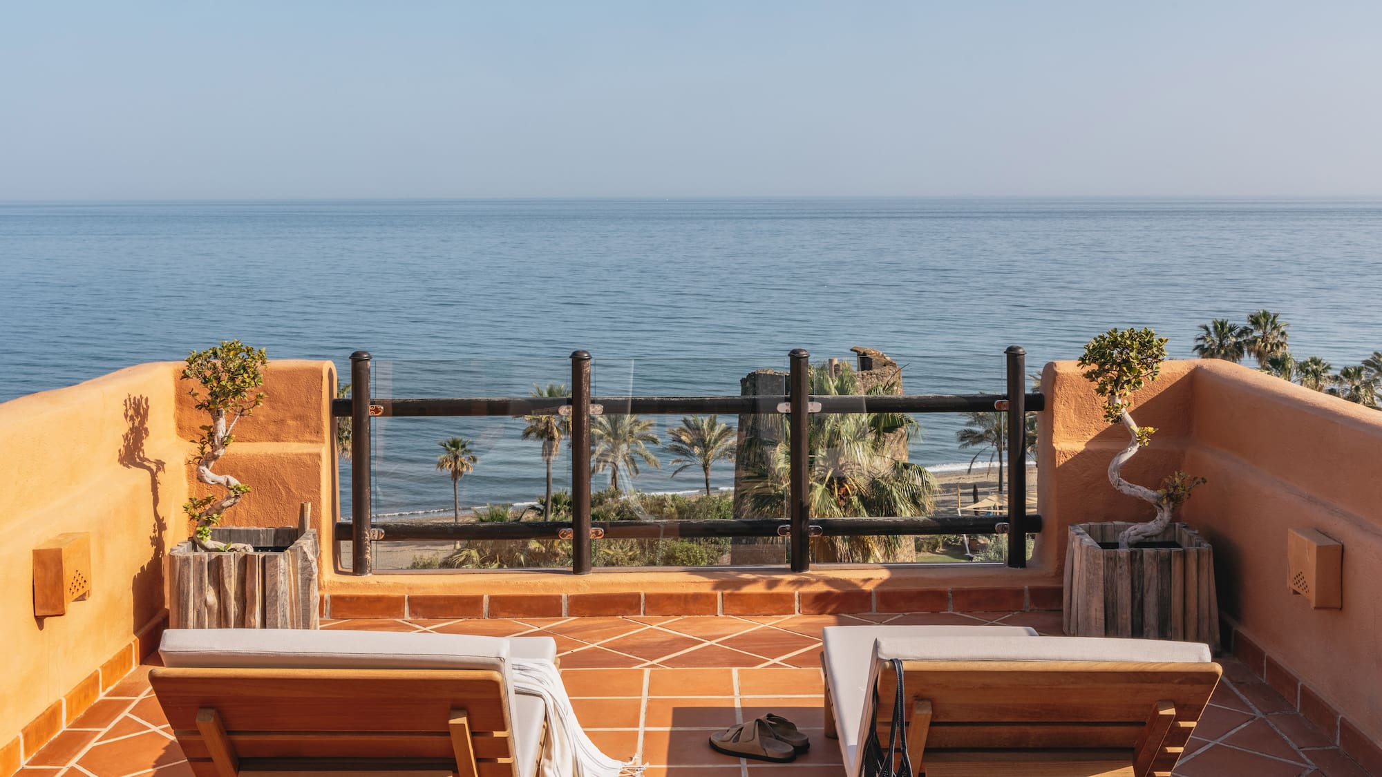 Oceanfront balcony with lounge chairs, palm trees, and beach view.