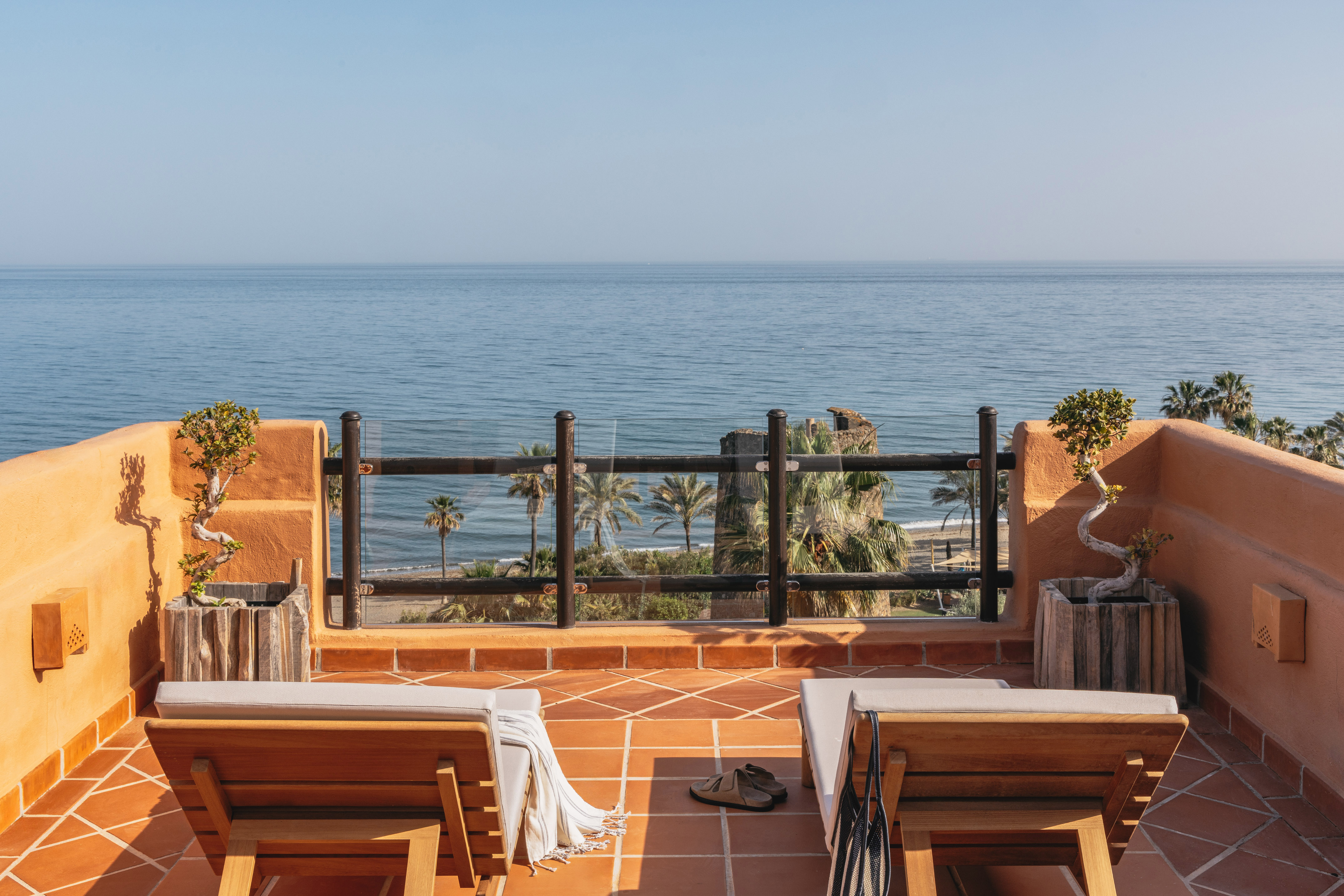 Oceanfront balcony with lounge chairs, palm trees, and beach view.