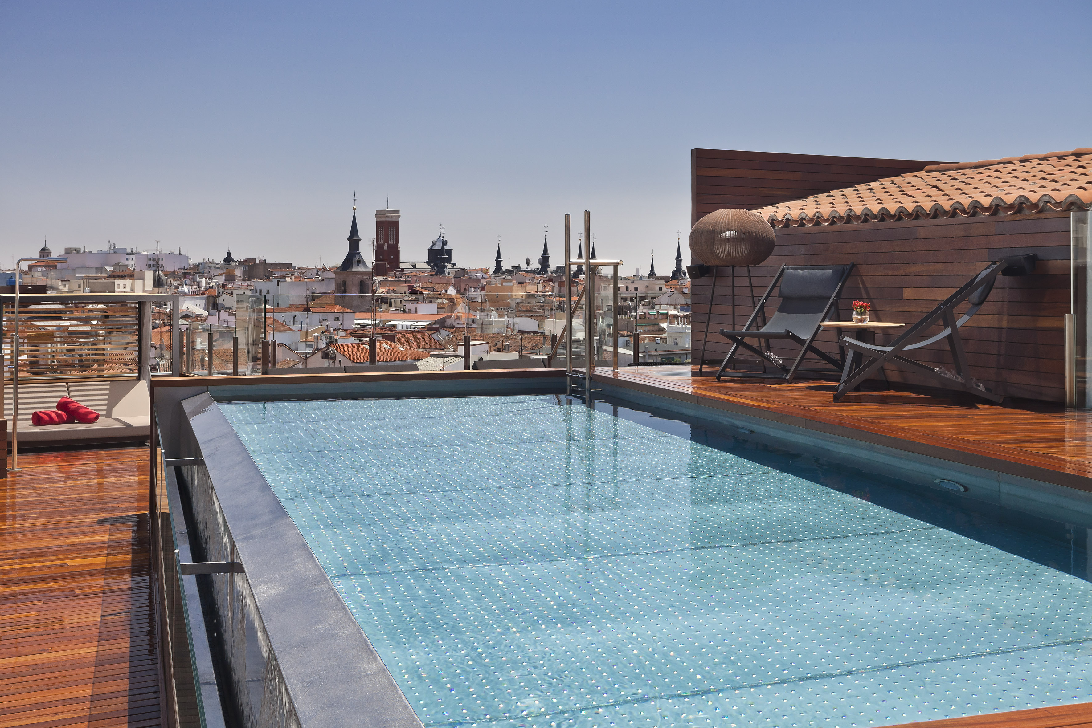 Rooftop pool with wooden deck, lounge chairs, Madrid city views.