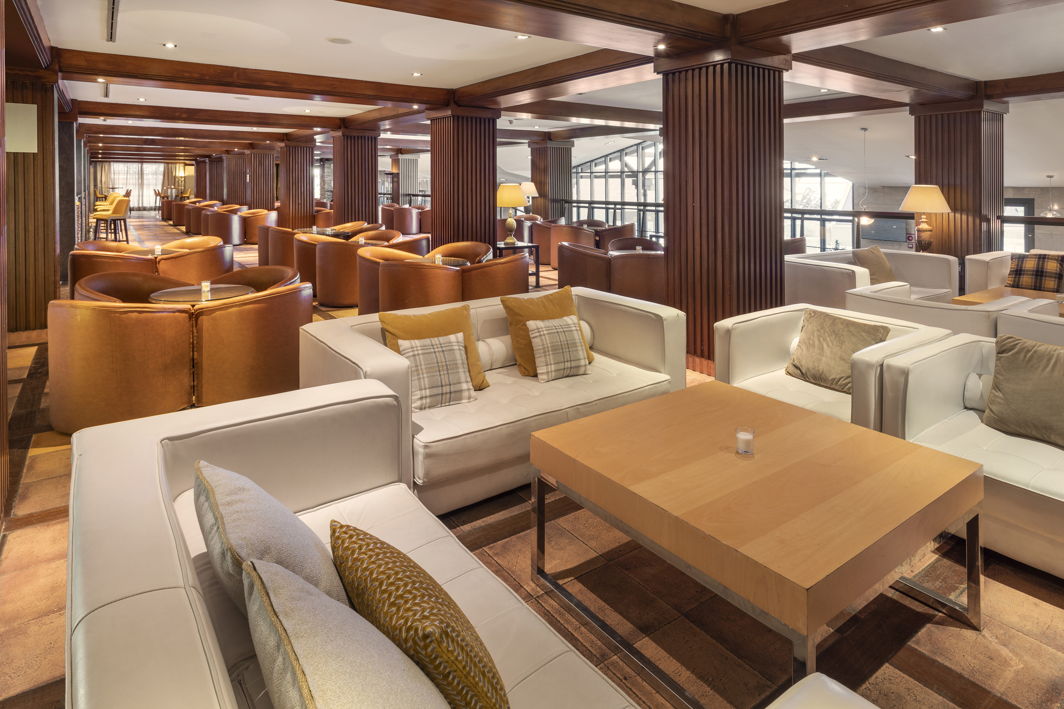 Hotel lounge: white sofas, brown leather chairs, wood columns, large windows.
