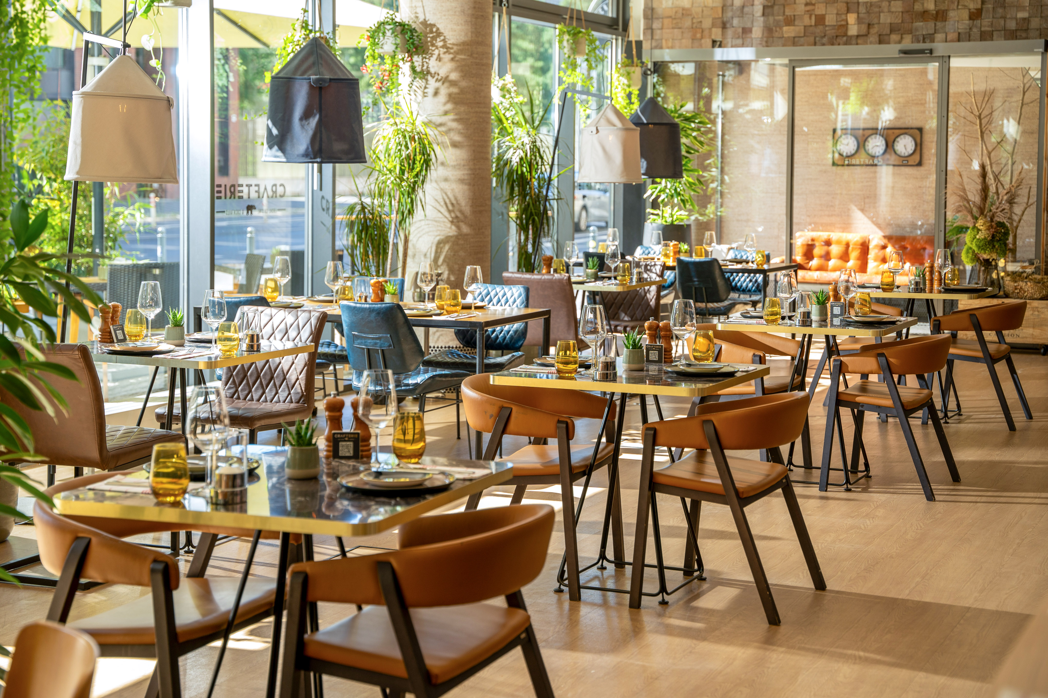 Modern restaurant interior with set tables, leather chairs, and green plants.