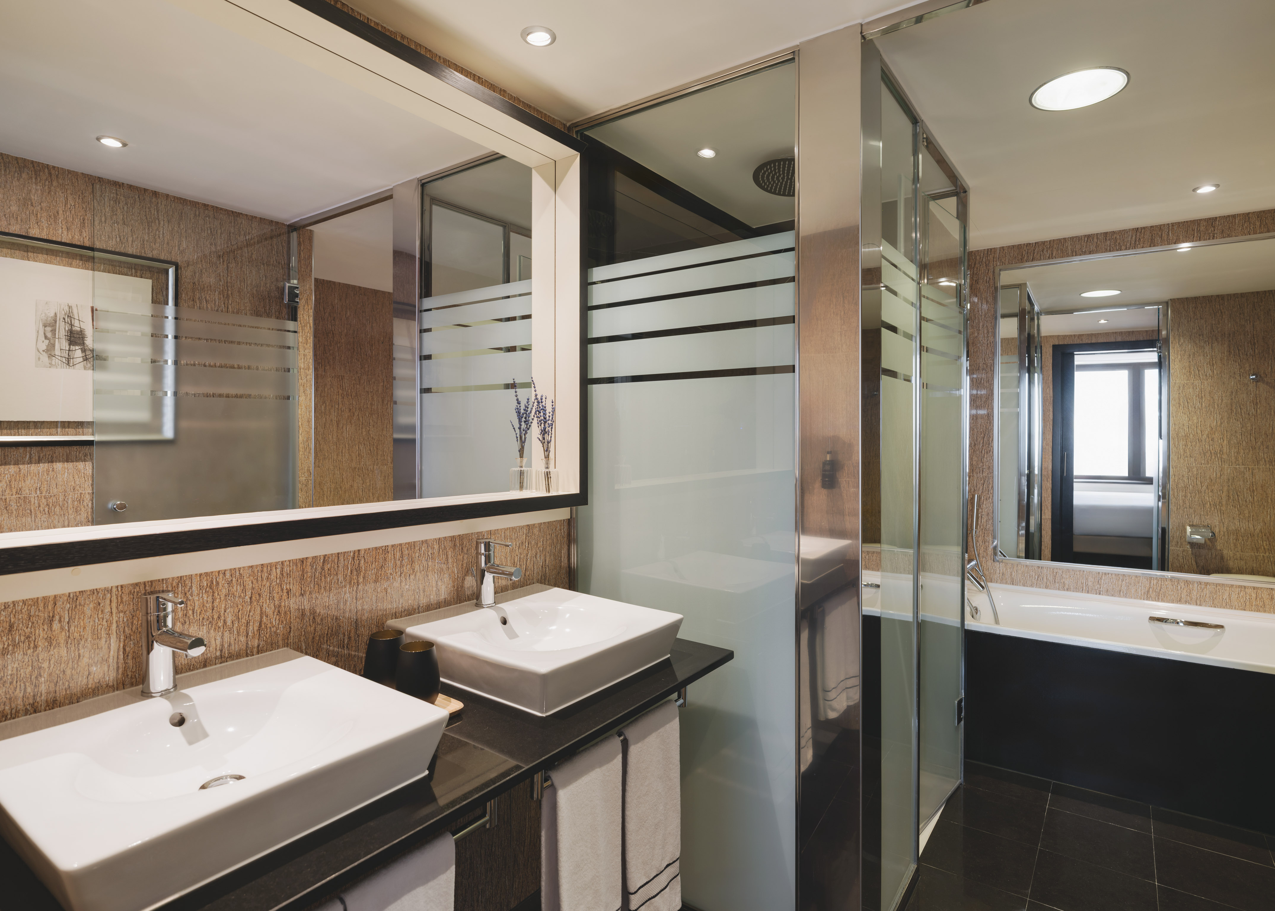 Elegante baño de hotel con doble lavabo, ducha de cristal y bañera.