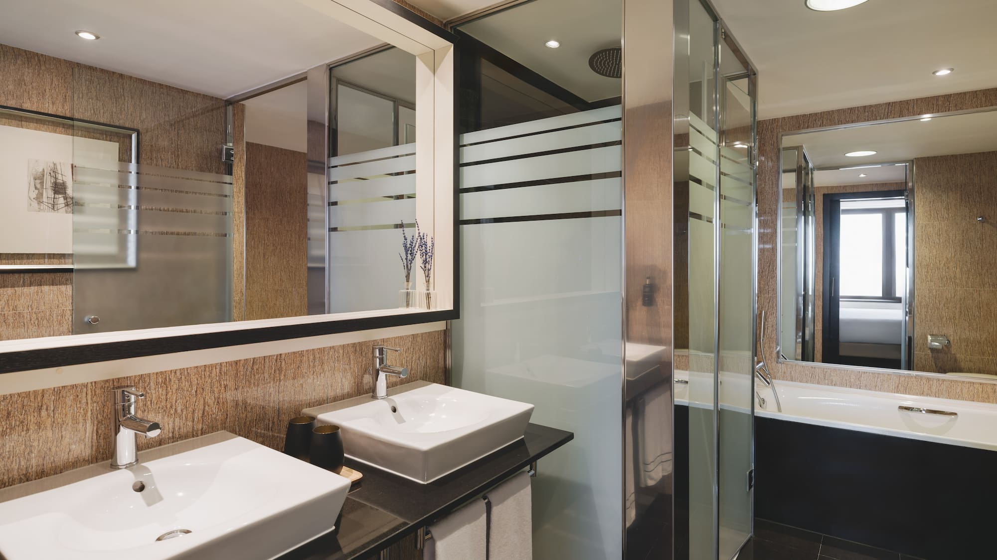 Elegante baño de hotel con doble lavabo, ducha de cristal y bañera.