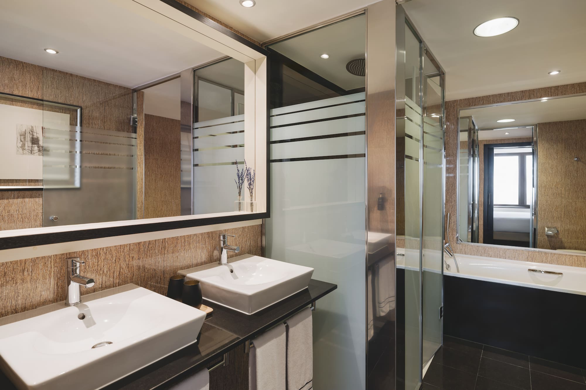 Elegante baño de hotel con doble lavabo, ducha de cristal y bañera.
