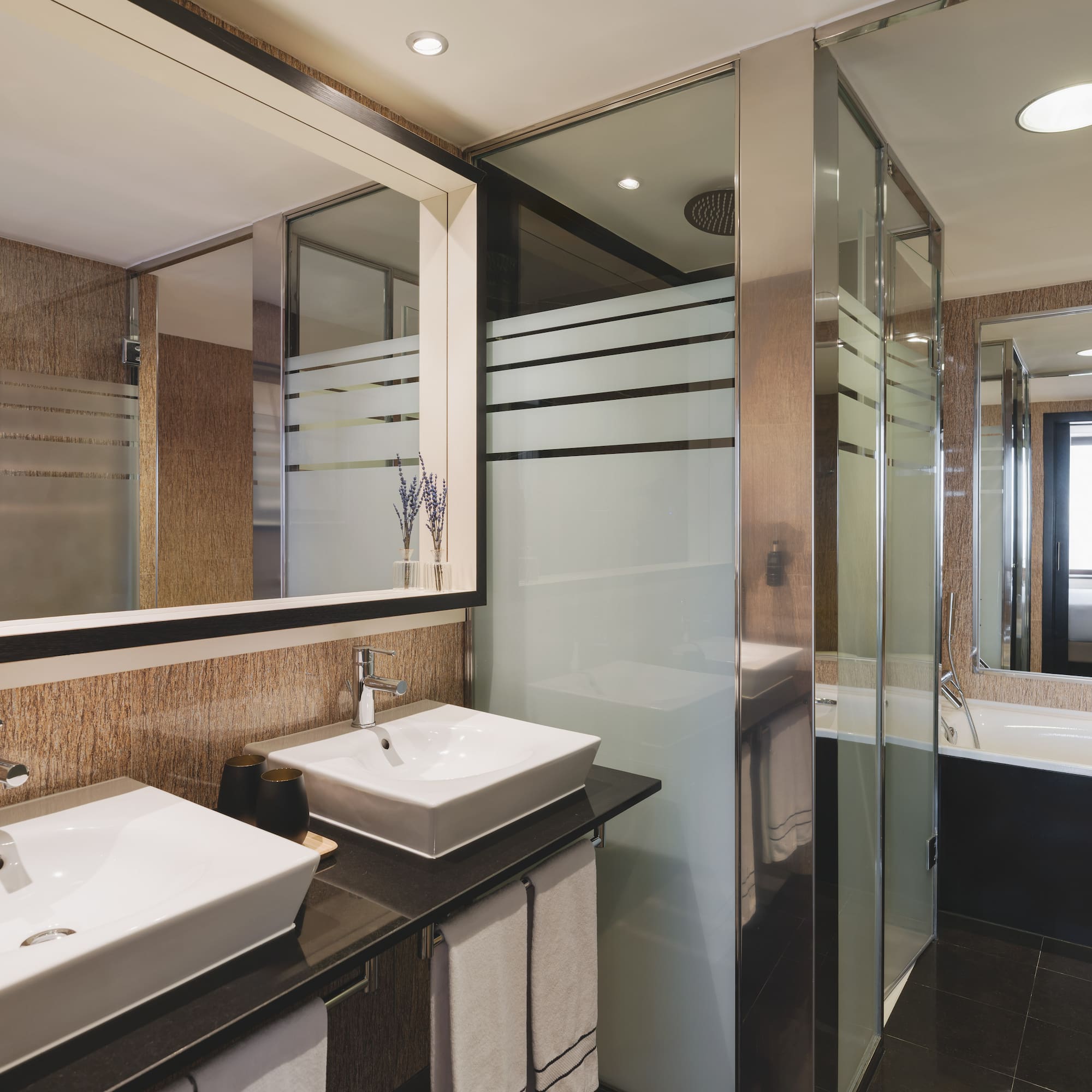 Elegante baño de hotel con doble lavabo, ducha de cristal y bañera.