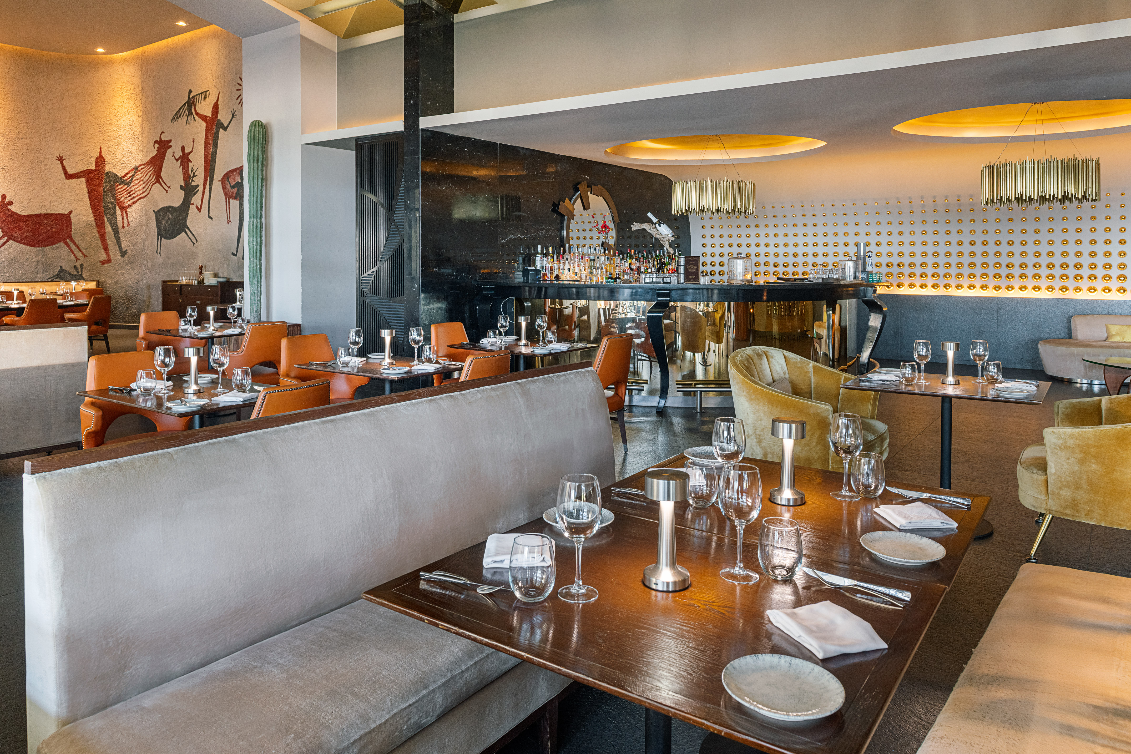 Modern restaurant interior with bar, set tables, booth seating, and wall mural.