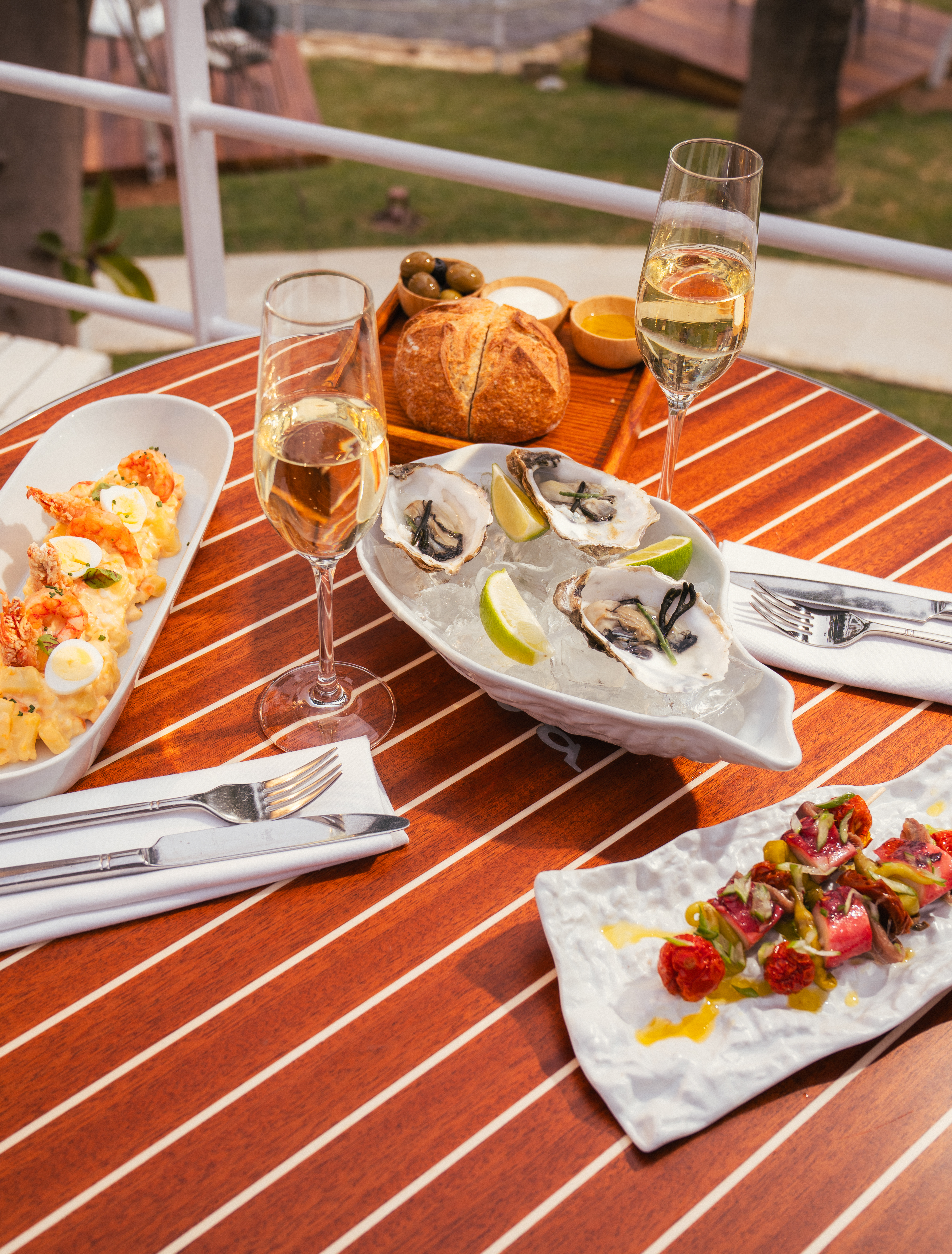 Oysters, shrimp, and champagne on a striped wooden table for outdoor dining.