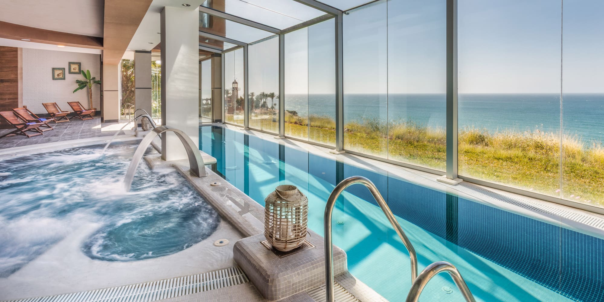 Indoor pool with hot tub, sea view, and lounge area at luxury spa.