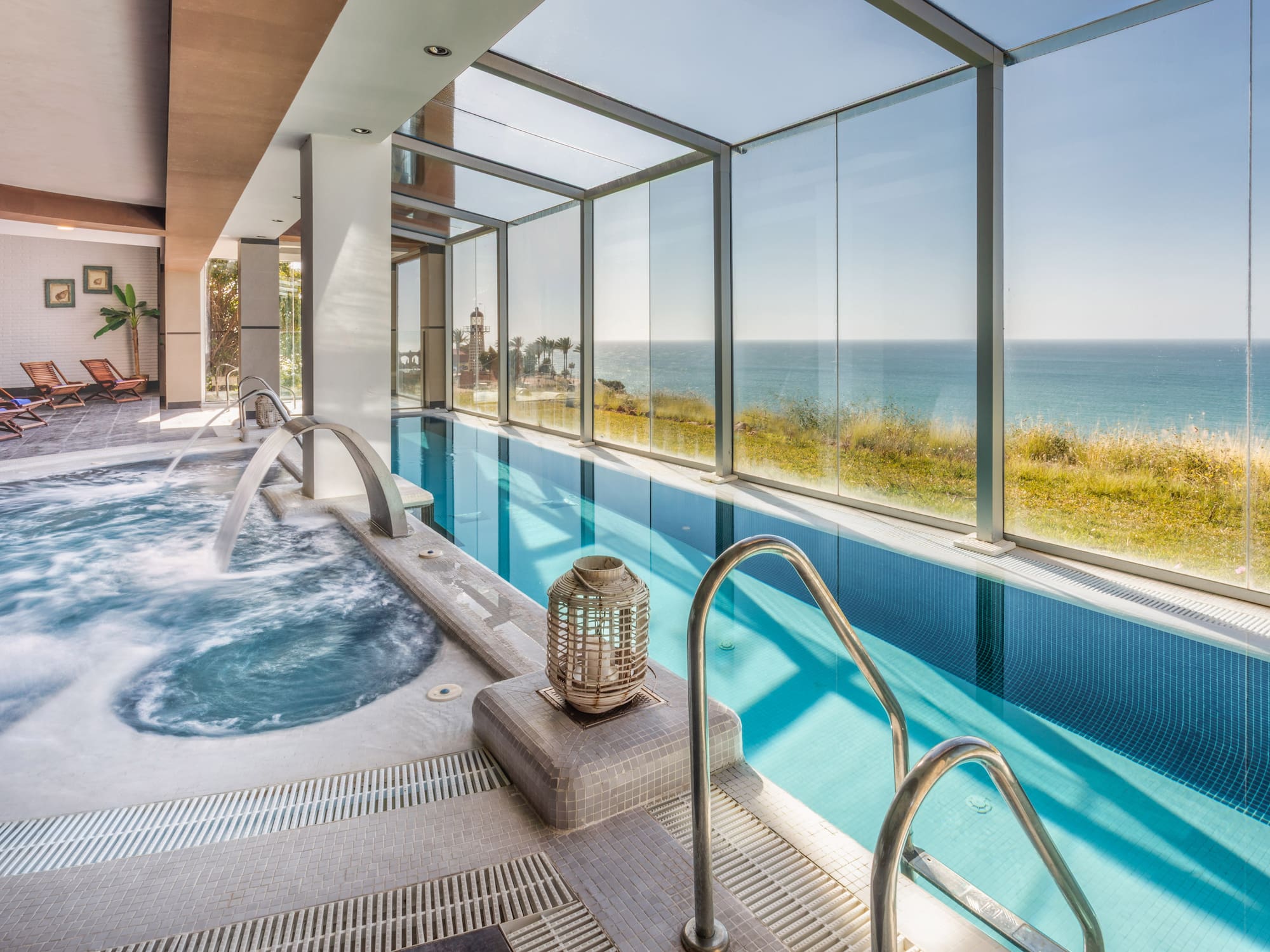 Coastal indoor swimming pool with sea view, jacuzzi, and relaxing lounge area.