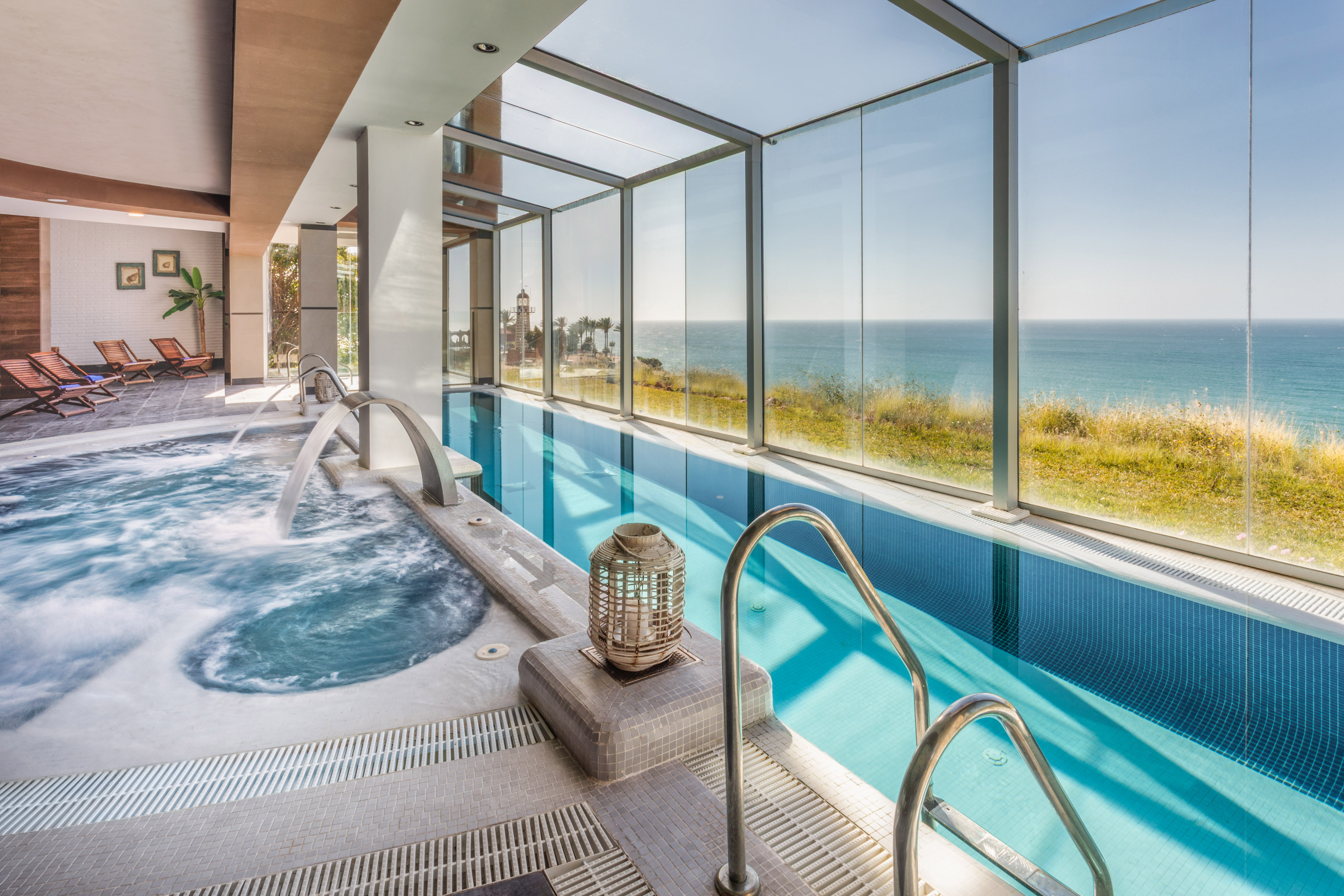 Coastal indoor swimming pool with sea view, jacuzzi, and relaxing lounge area.