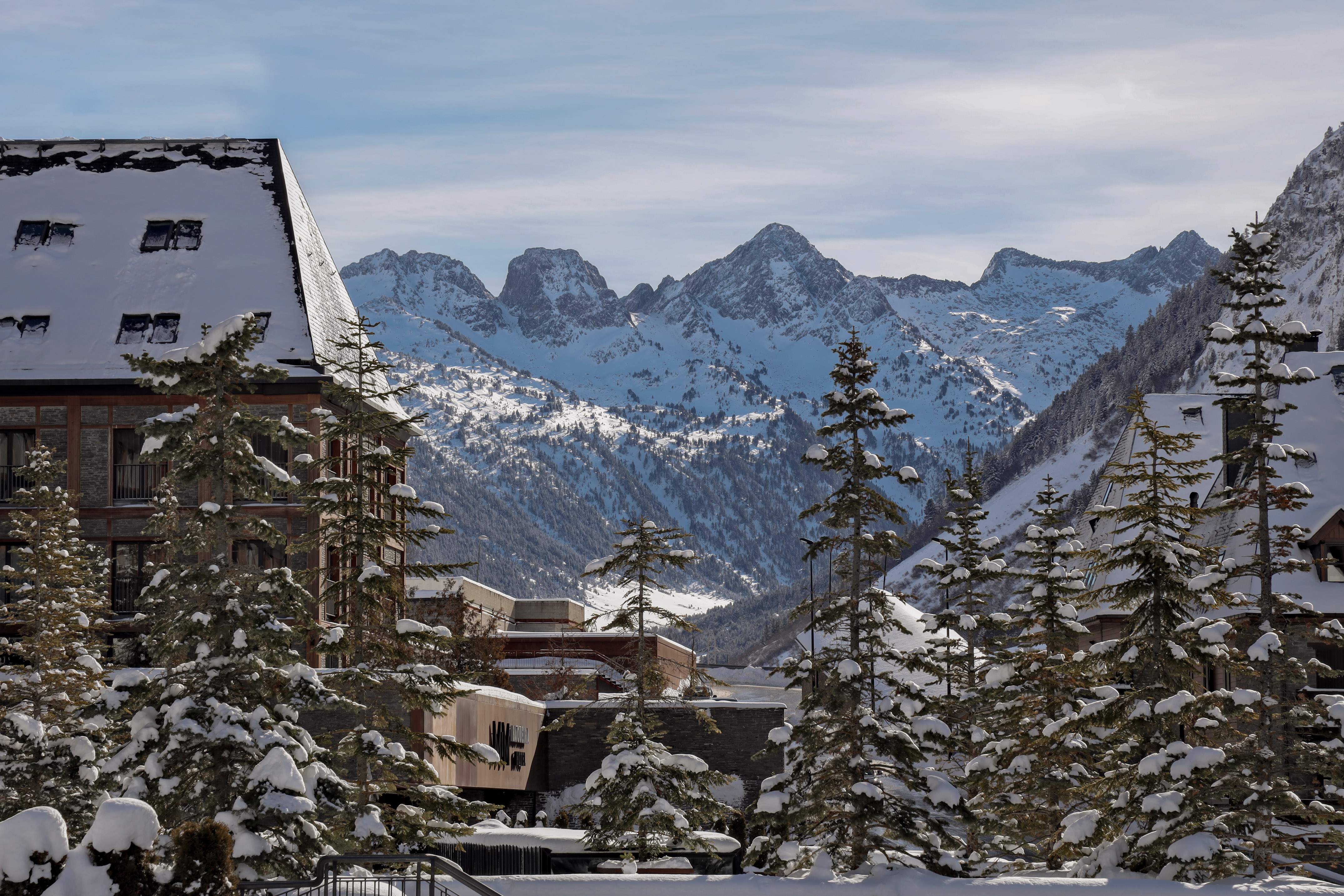 Snowy alpine resort with snow-covered buildings, pine trees, and mountains.