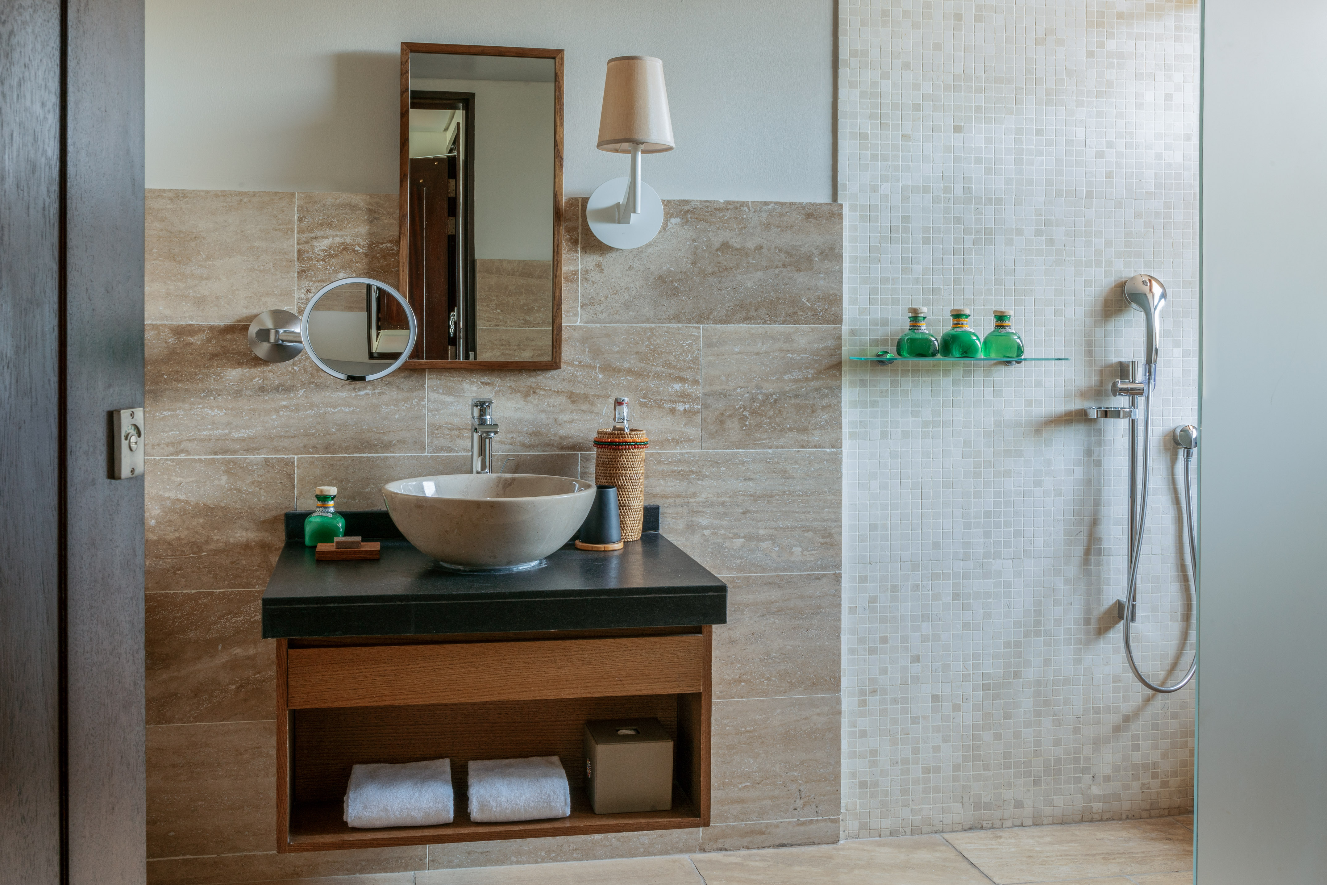 Modern bathroom with stone vessel sink, wood mirror, tiled shower.