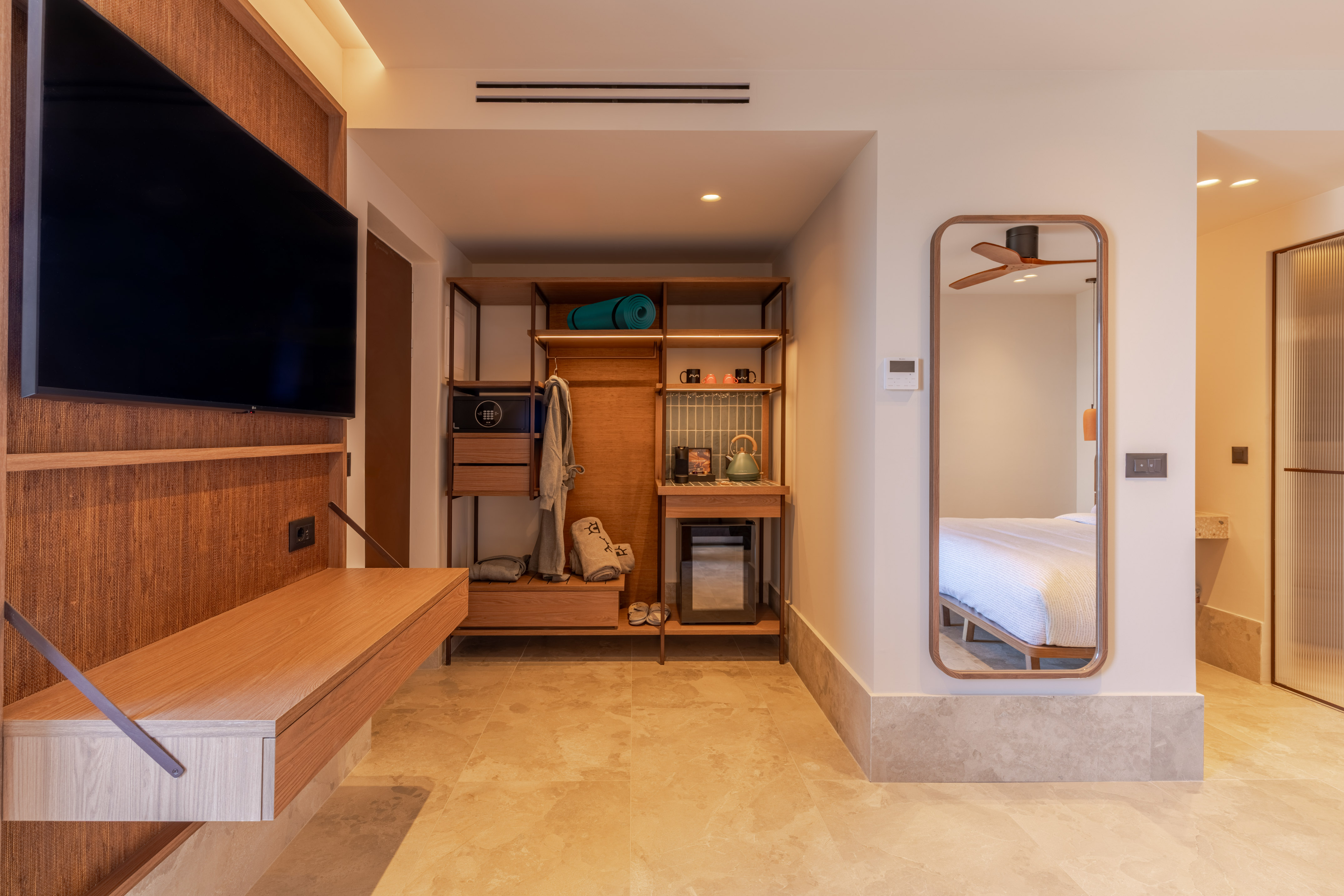 Modern hotel room entry with TV, open wardrobe, mini-fridge, and full-length mirror.