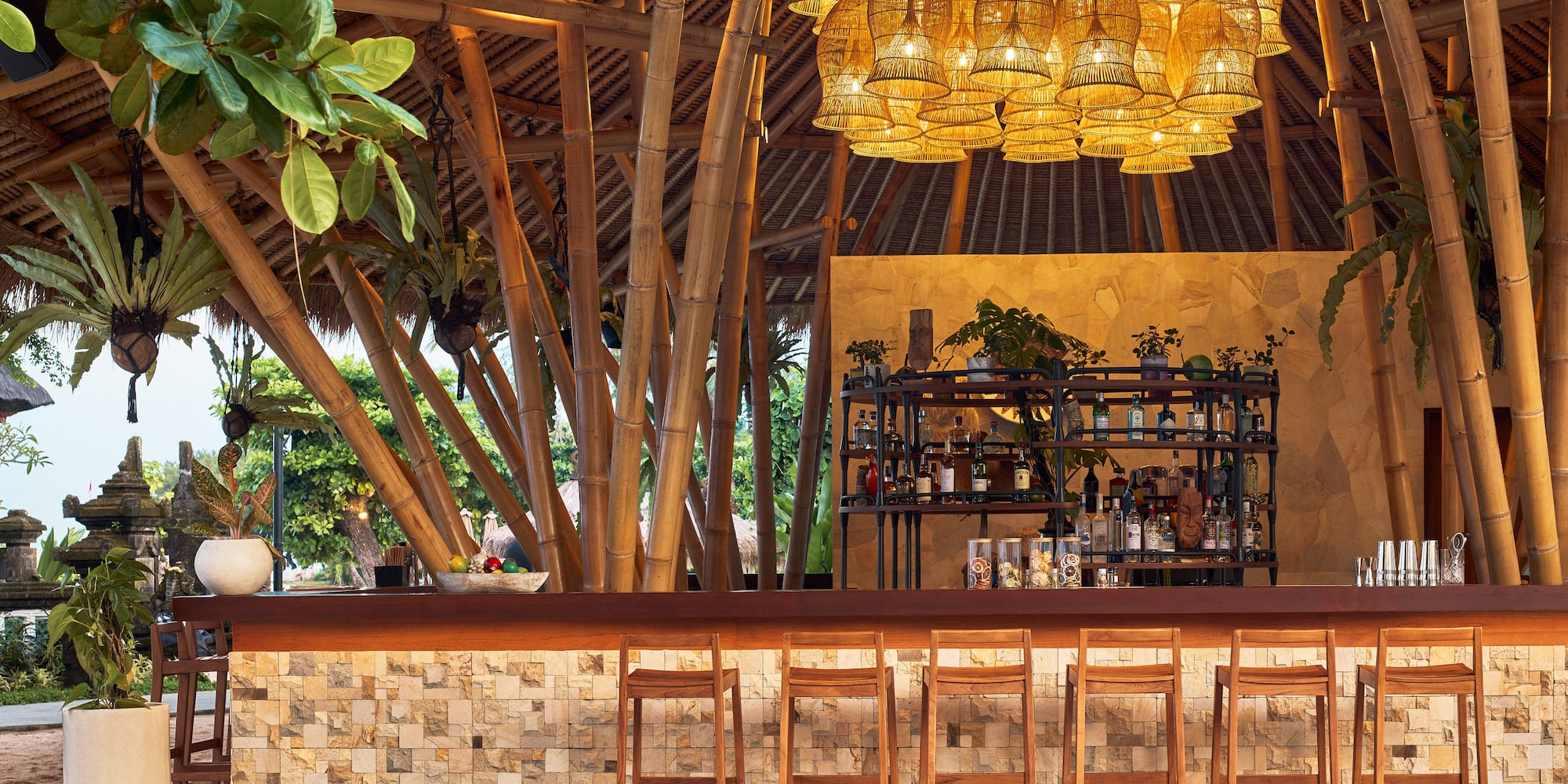 Tropical bamboo bar with rattan lights, stone accents, and wooden stools.