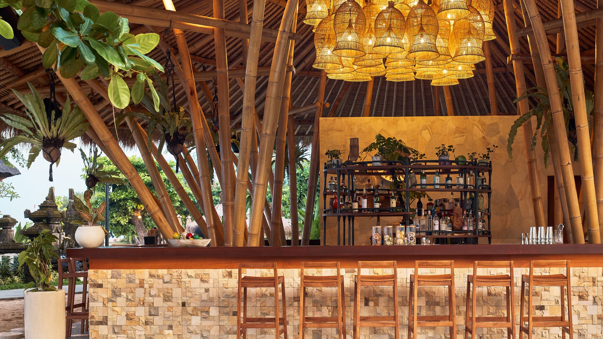 Tropical bamboo bar with rattan lights, stone accents, and wooden stools.
