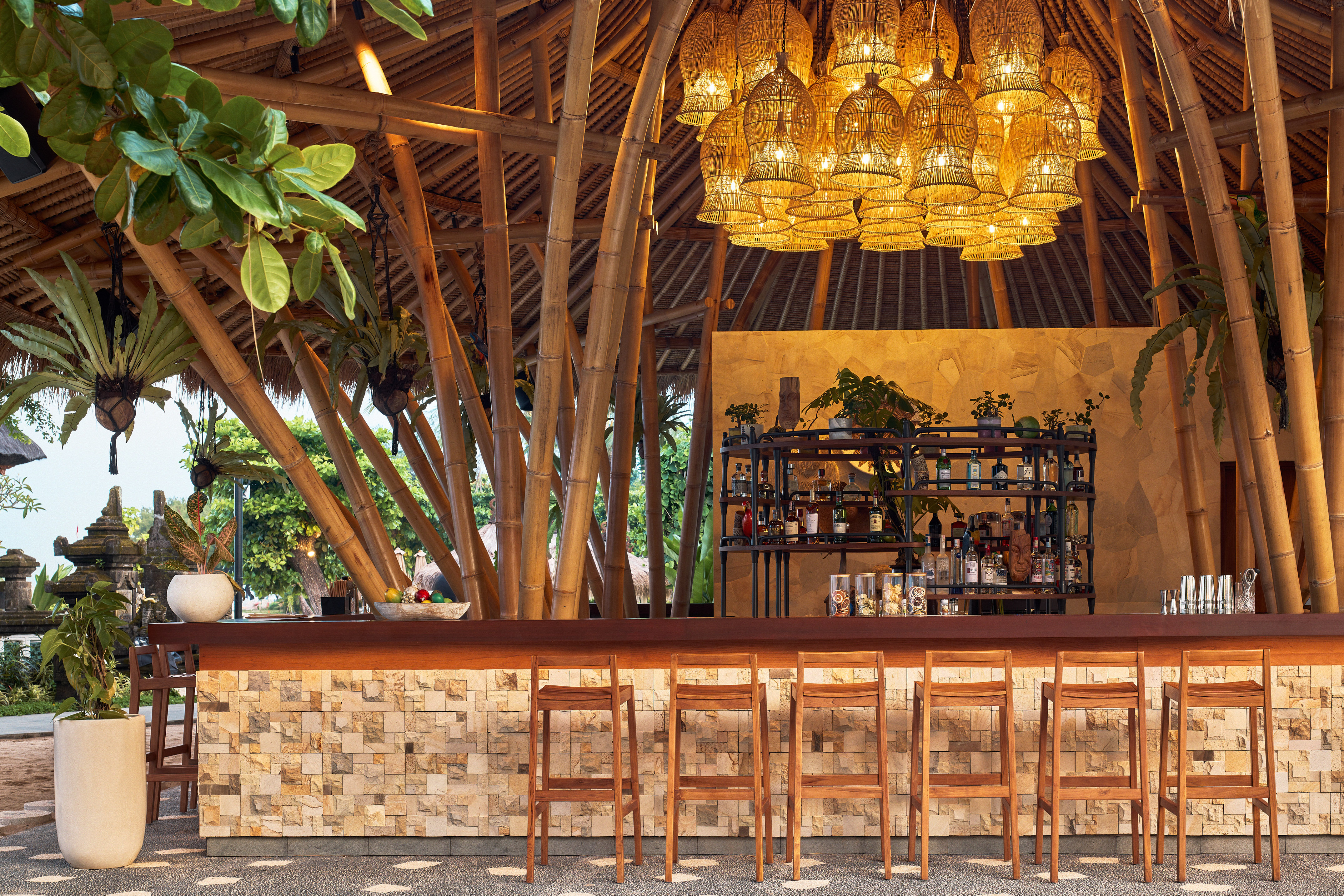 Tropical bamboo bar with rattan lights, stone accents, and wooden stools.