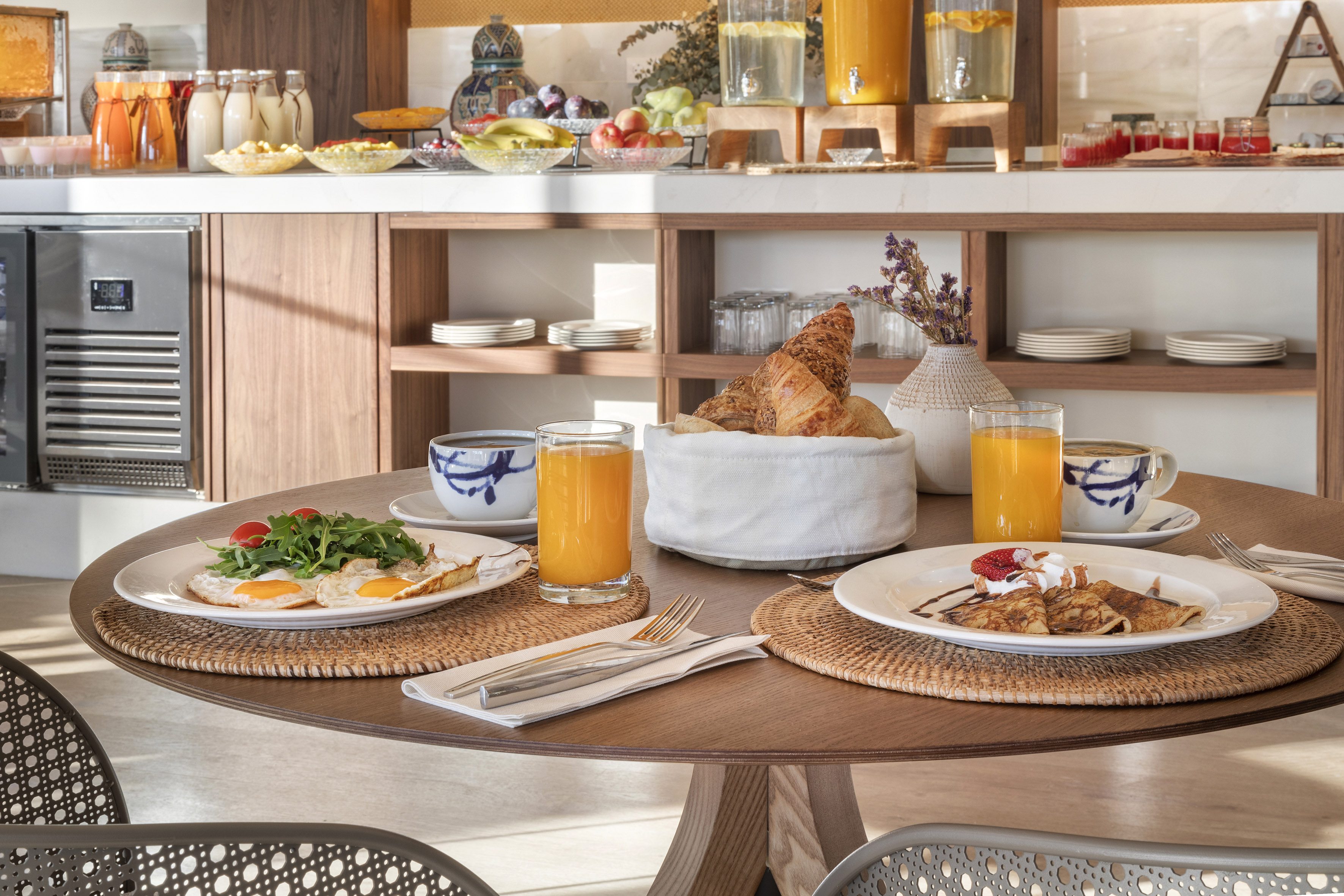 Hotel breakfast buffet with eggs, crepes, juice, and fresh pastries on a wooden table.