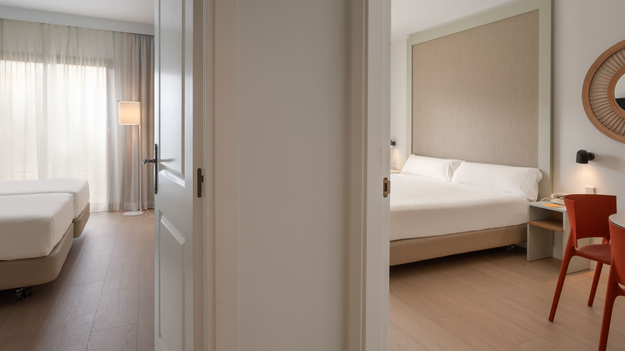 Open door connecting two modern hotel bedrooms with beds and wooden floors.