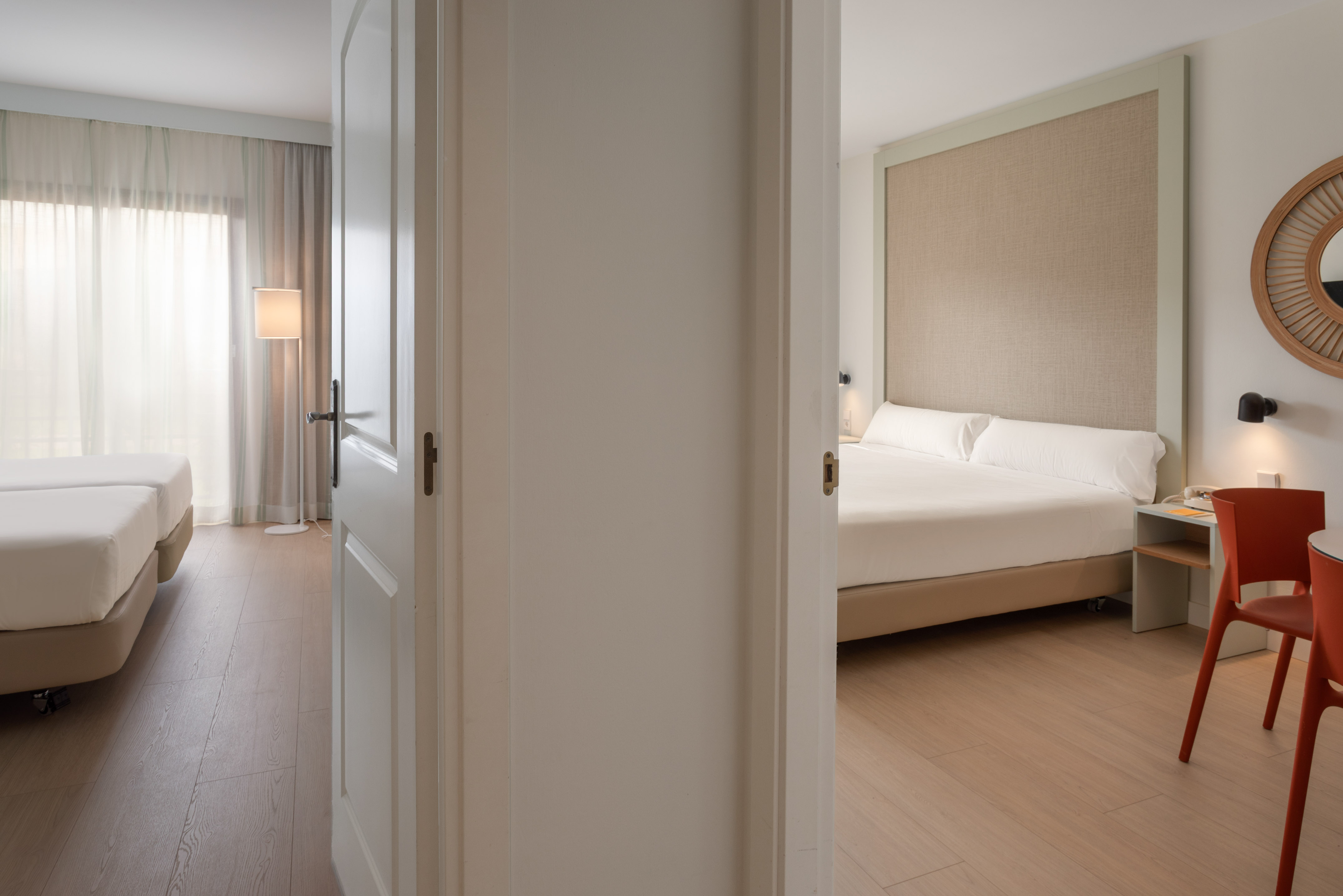 Open door connecting two modern hotel bedrooms with beds and wooden floors.