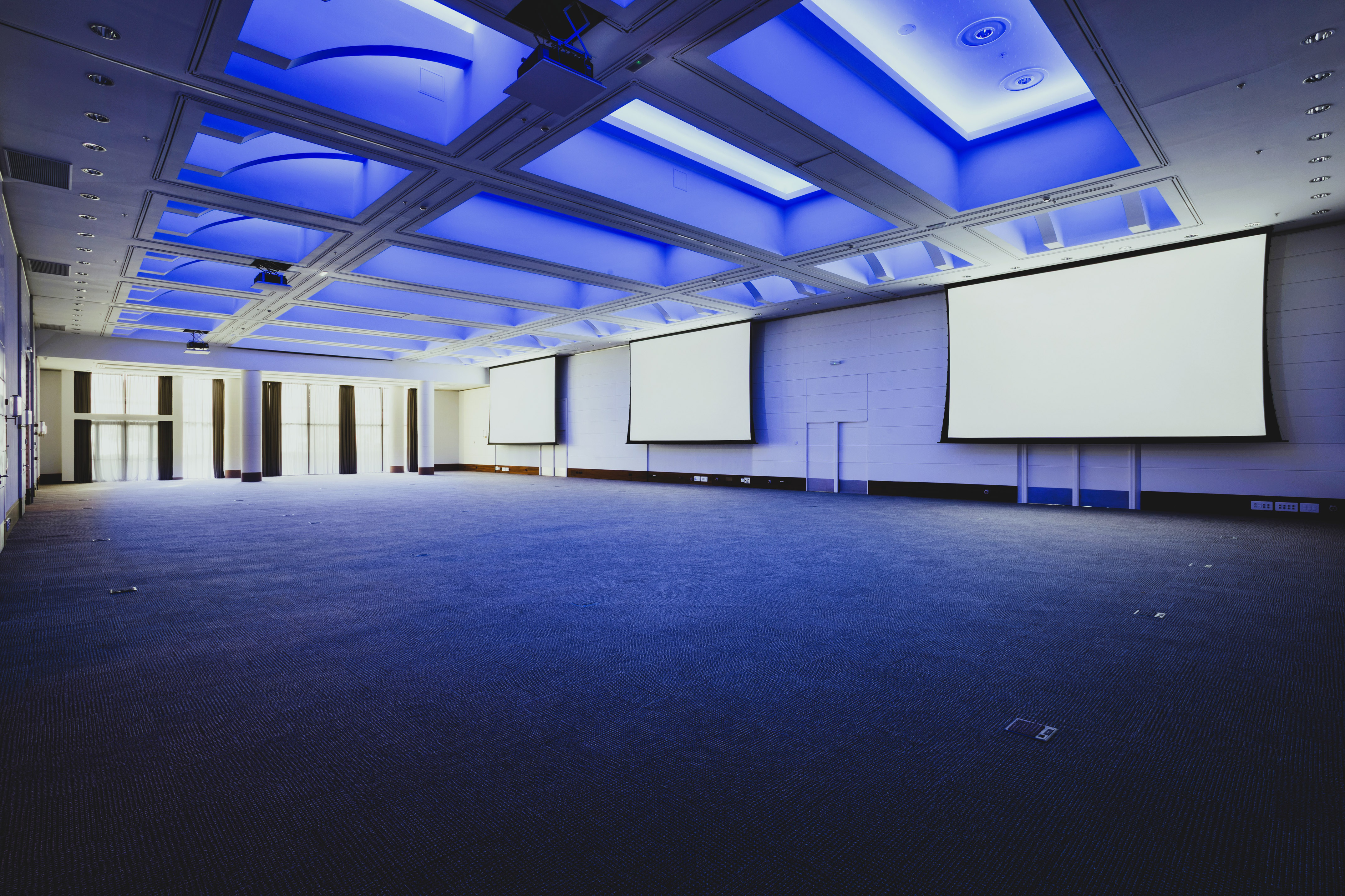 Empty conference room with blue ceiling lights and three projection screens.