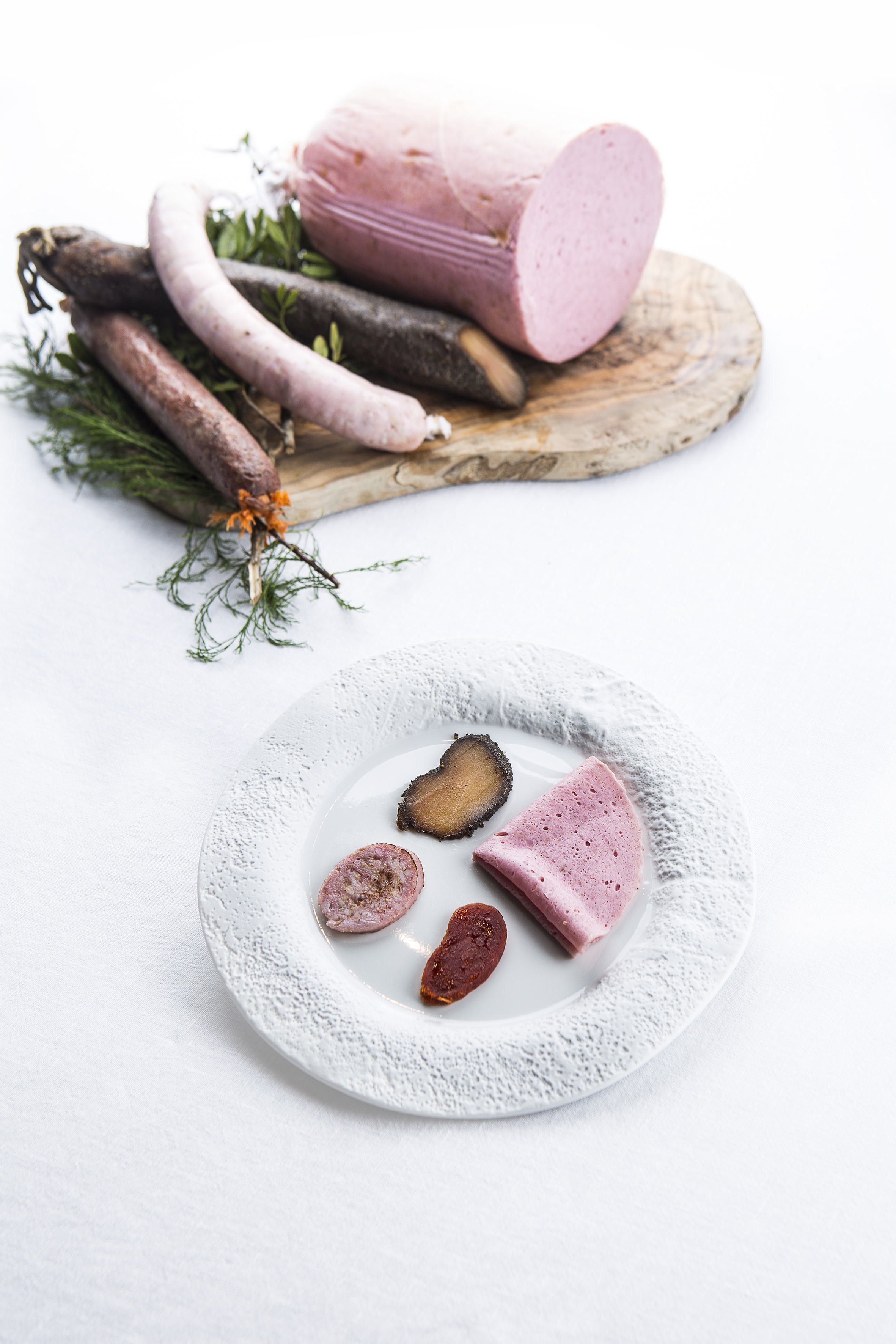 Whole sausages, pink bologna loaf, and sliced charcuterie on a plate.