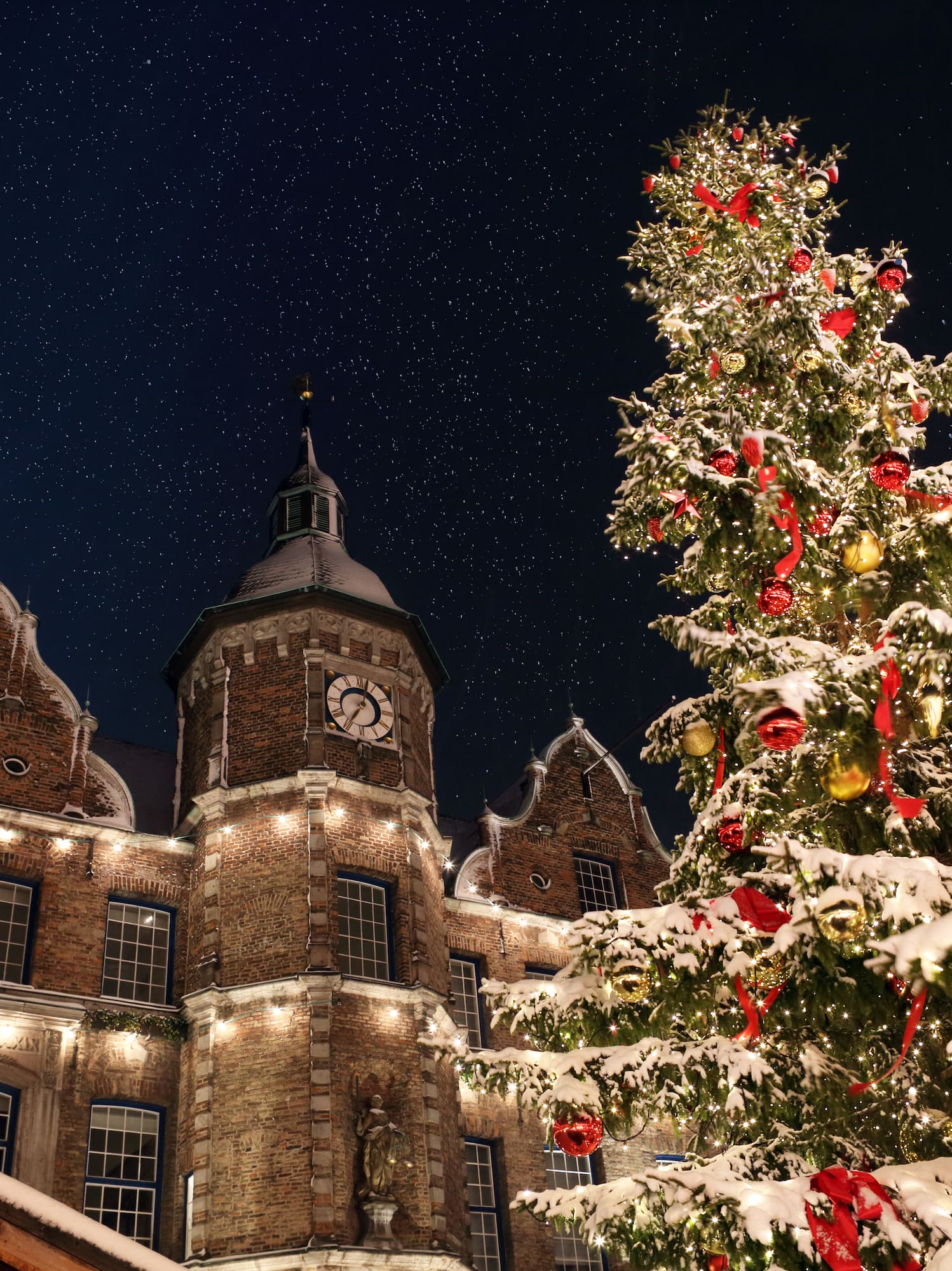 Snowy Christmas tree with ornaments, historic clock tower, and starry night sky.