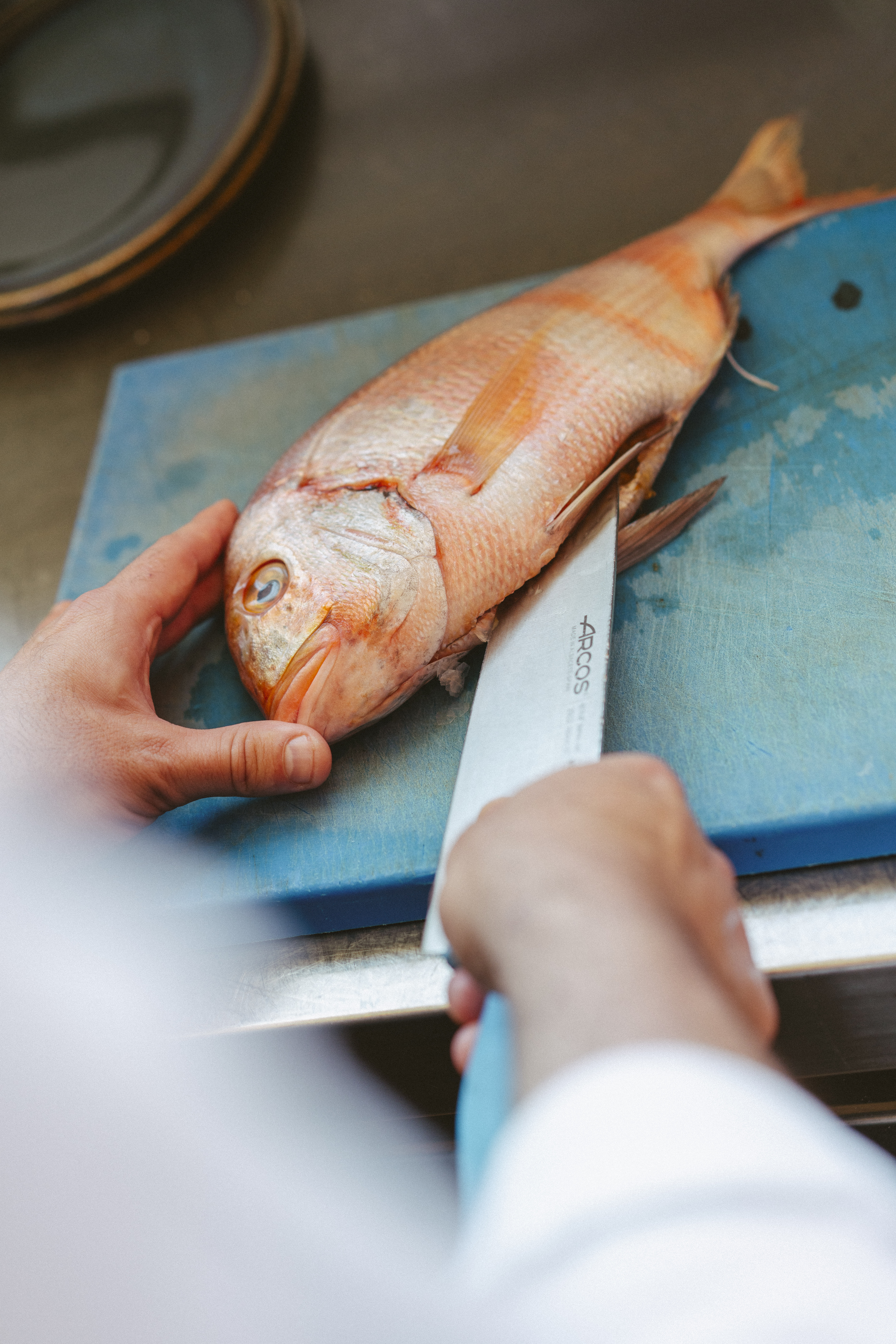 Chef preparing fresh red snapper with knife on blue cutting board.