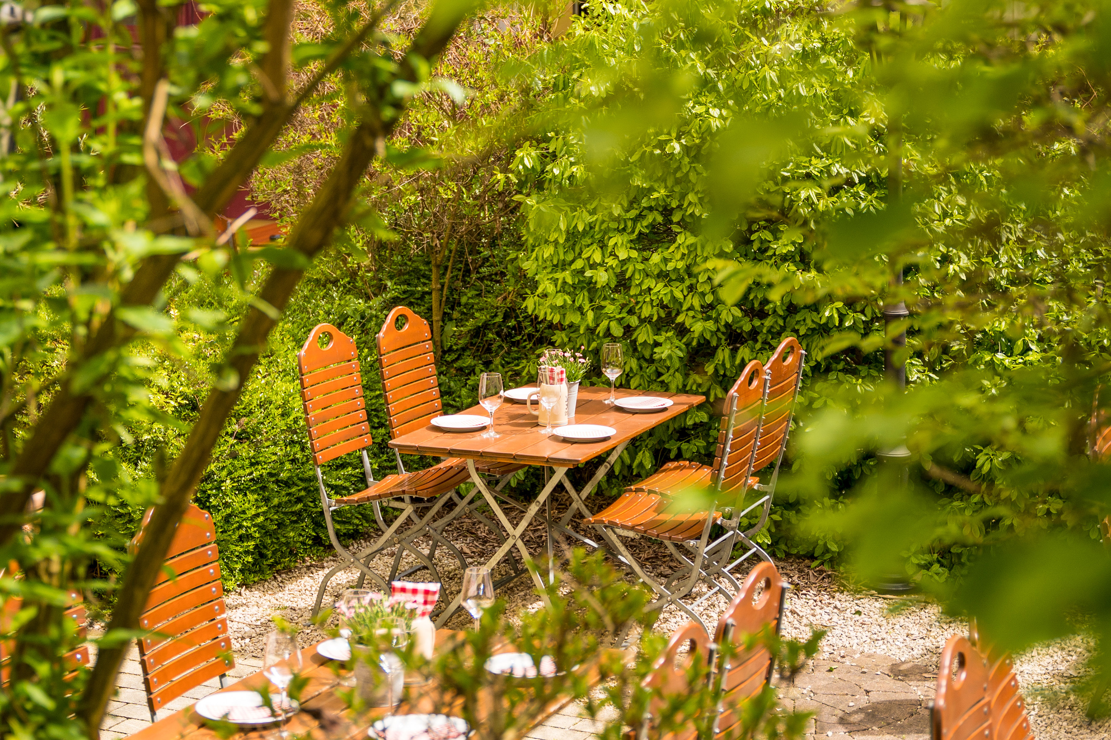Beer garden patio with wooden table, chairs, and lush green foliage.