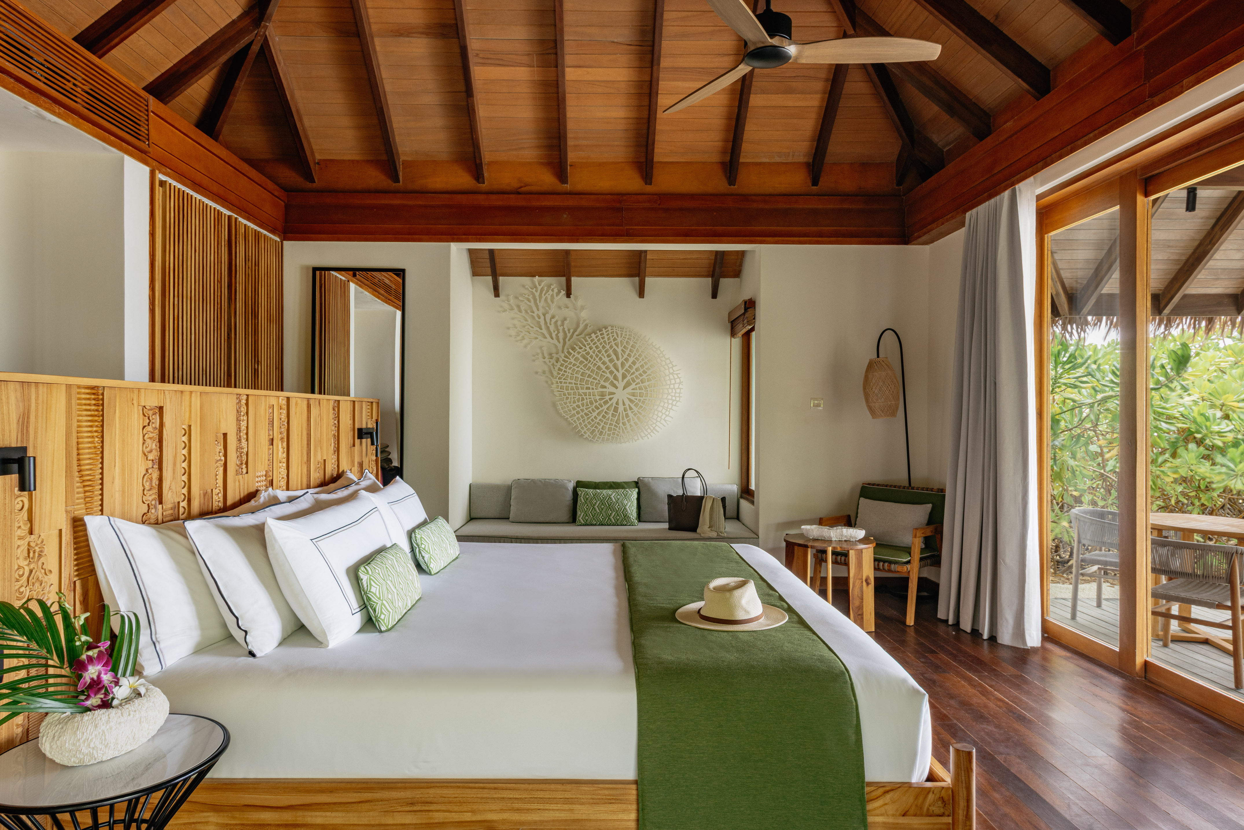 Tropical luxury bedroom with wood ceiling, large bed, green linens, and balcony.