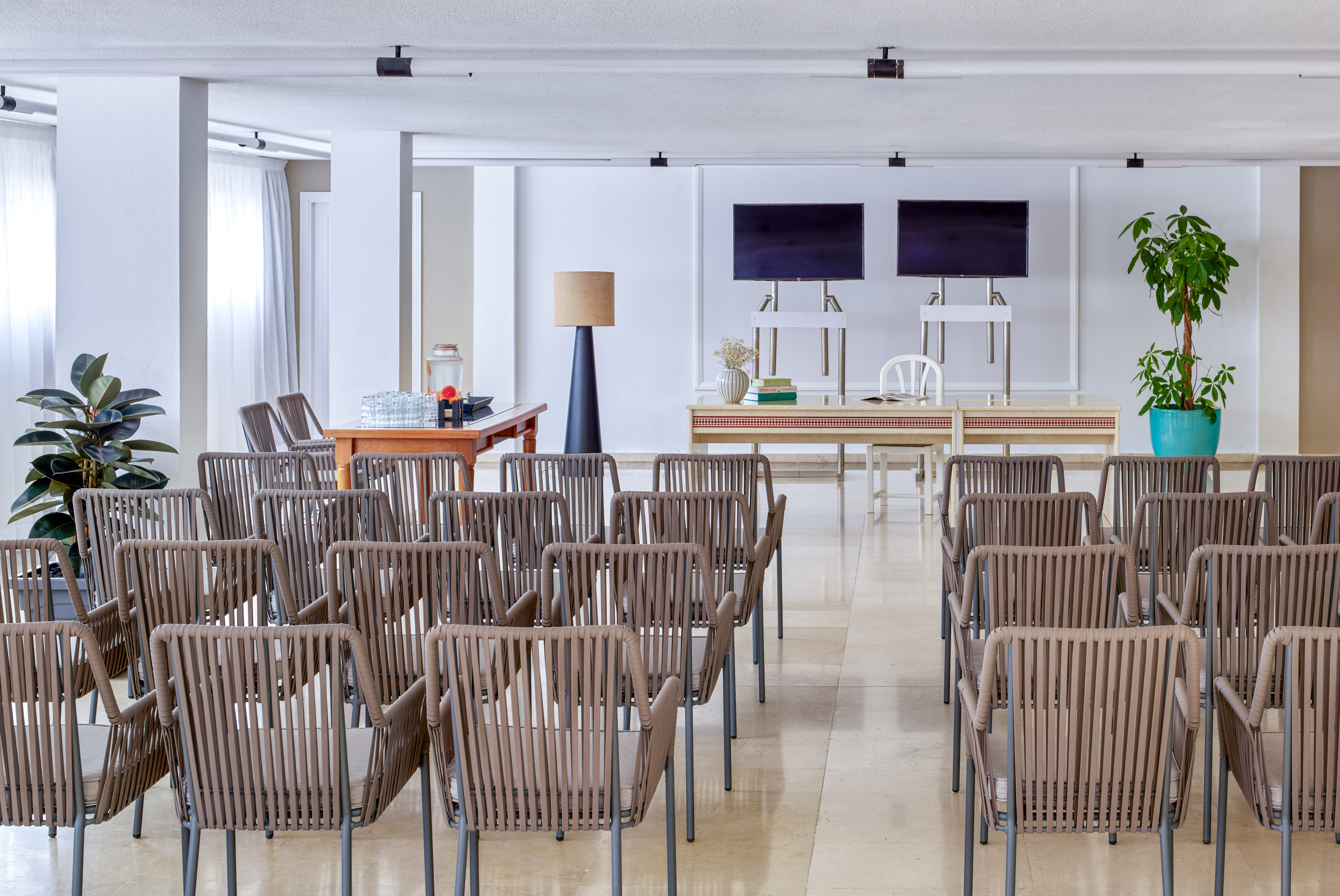 Modern conference room with rows of chairs, screens, and refreshment station.