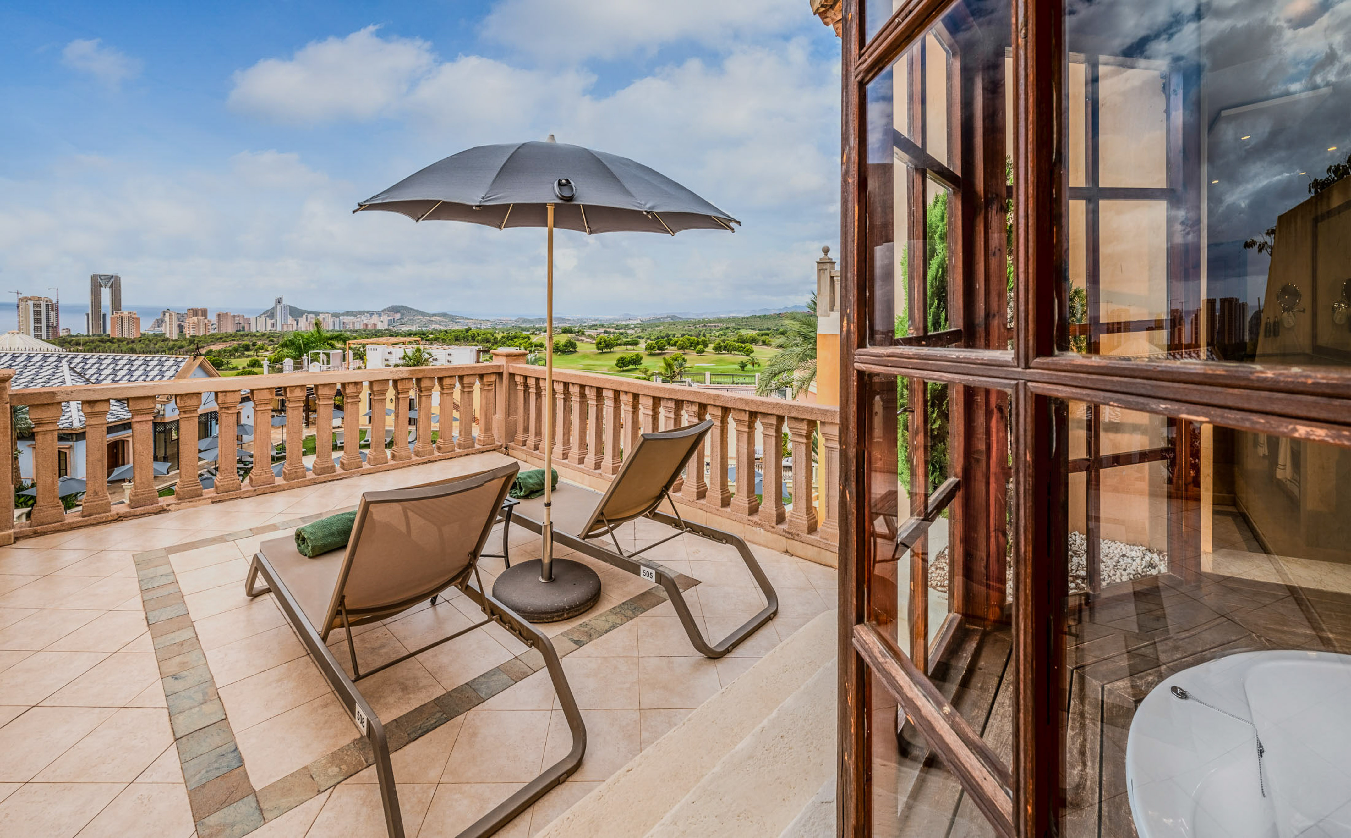 Balcony with lounge chairs, umbrella, golf course, and Benidorm city view