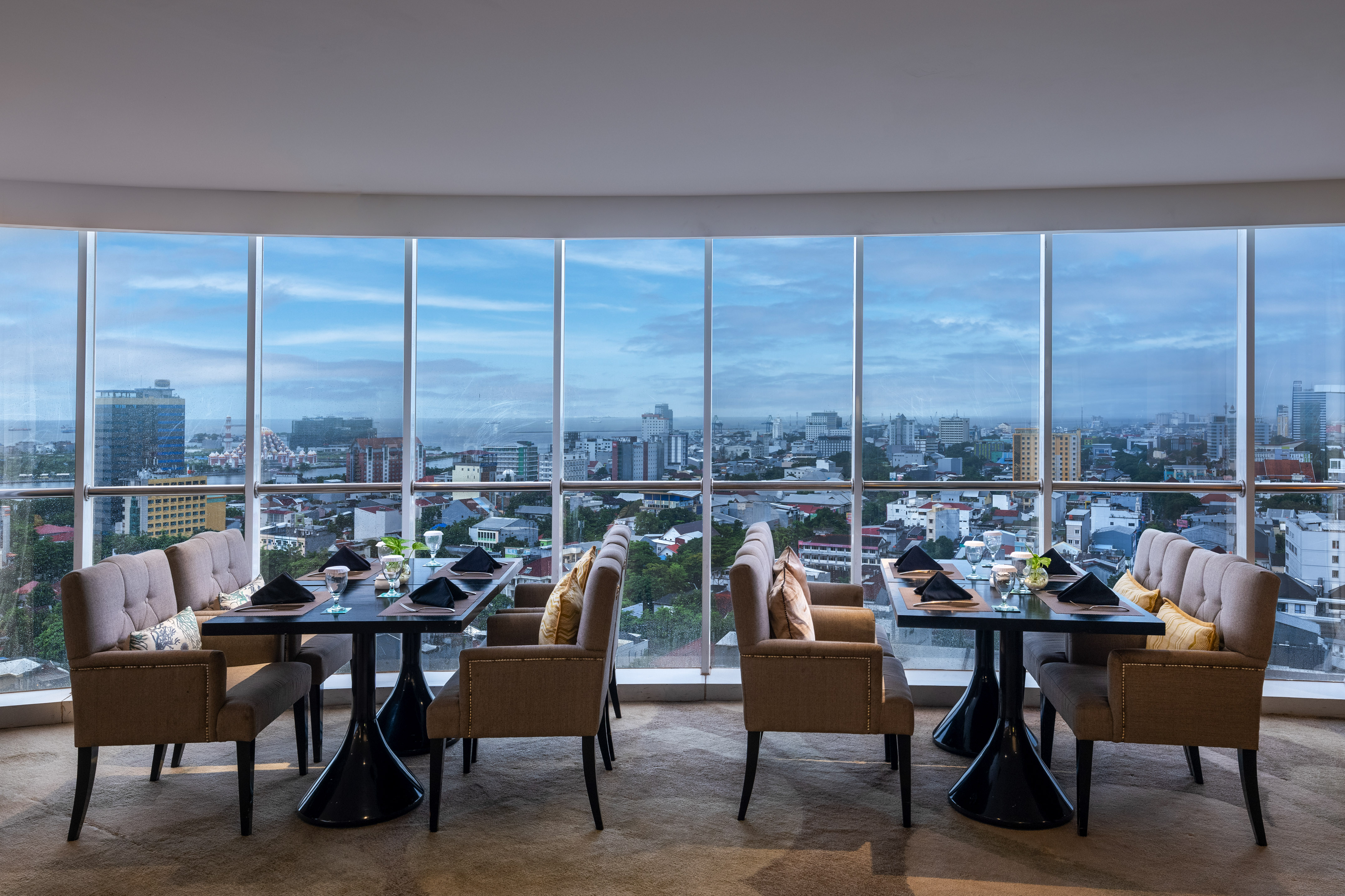 Restaurant dining room with set tables and panoramic city skyline view.