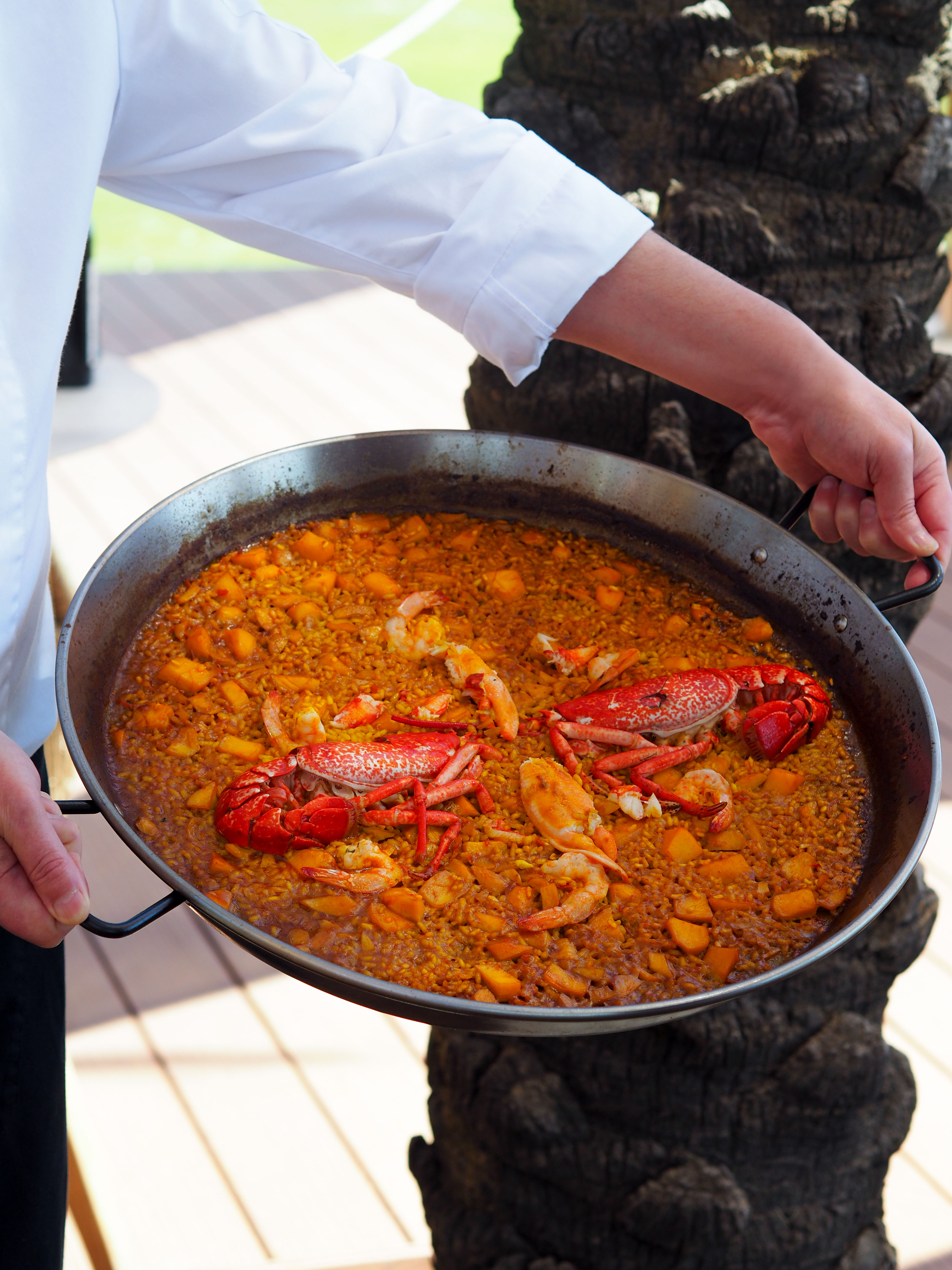 Seafood paella with lobster and shrimp in a large pan held by a chef.