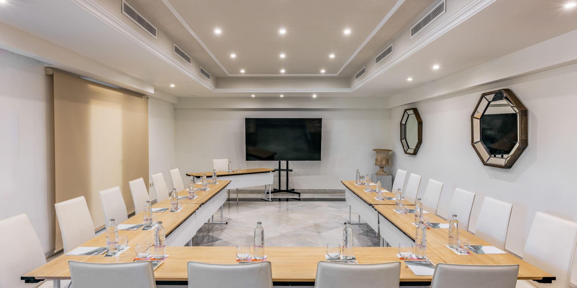 Sleek U-shape meeting room with white chairs, large TV screen, and recessed lighting.