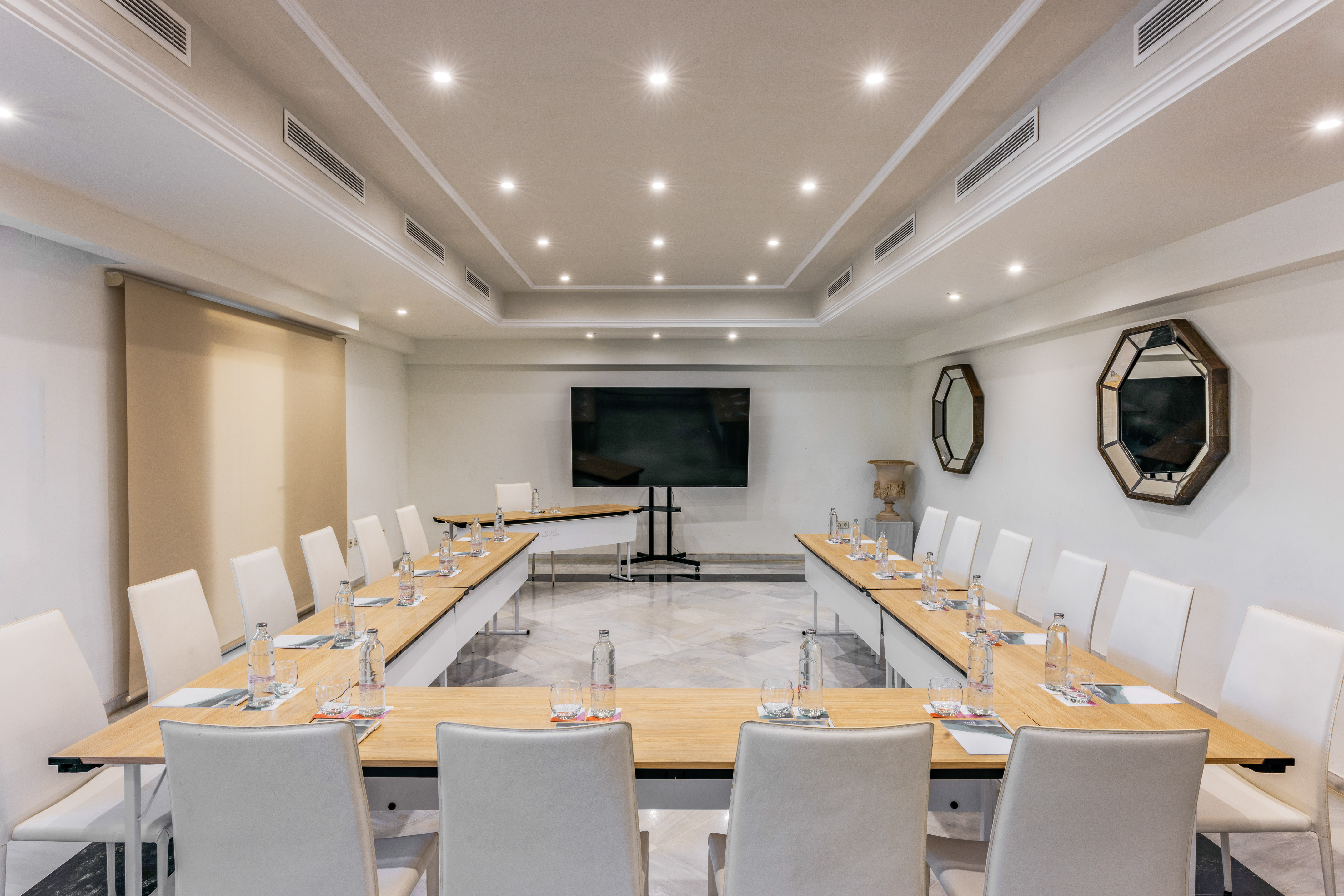 Sleek U-shape meeting room with white chairs, large TV screen, and recessed lighting.