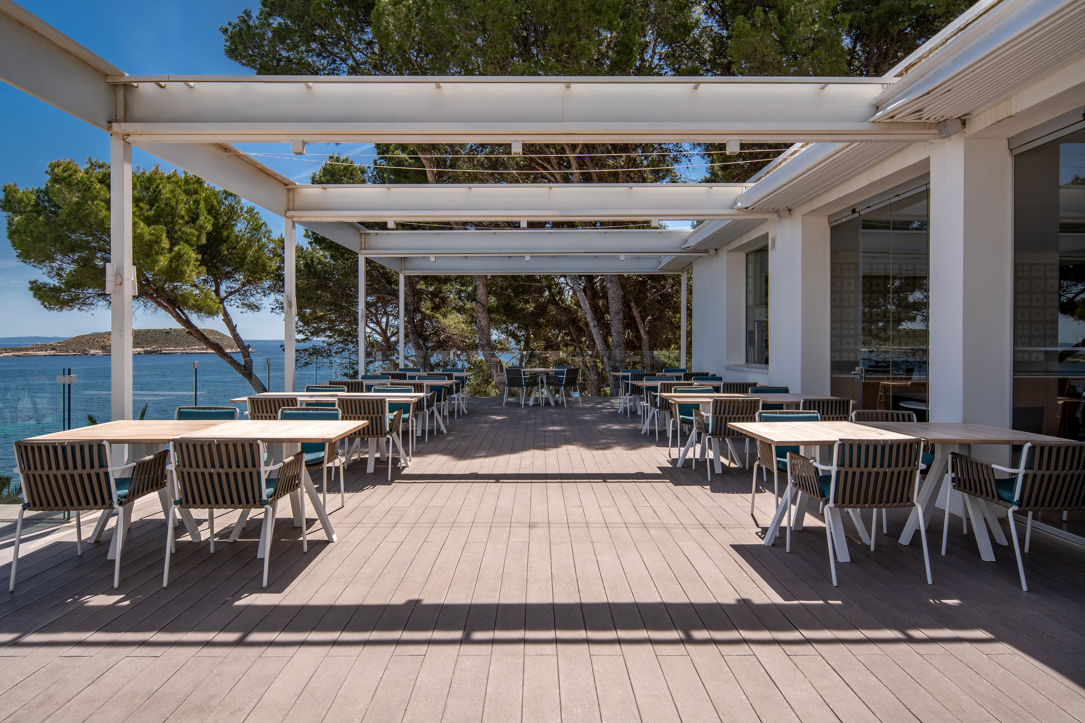 Modern outdoor restaurant terrace with sea view, tables, and white pergola.