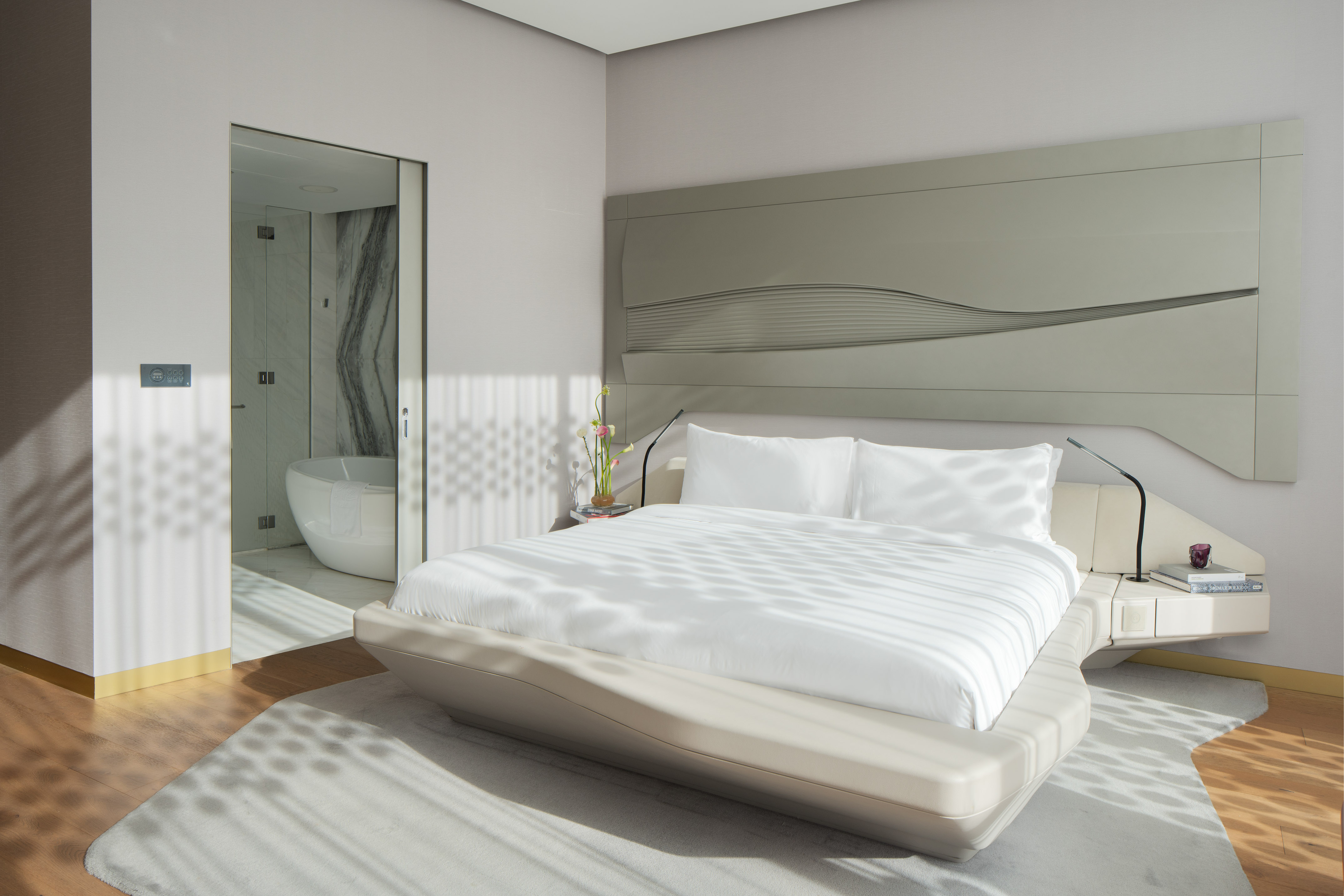 Modern bedroom with white bed, abstract headboard, and ensuite bathroom.