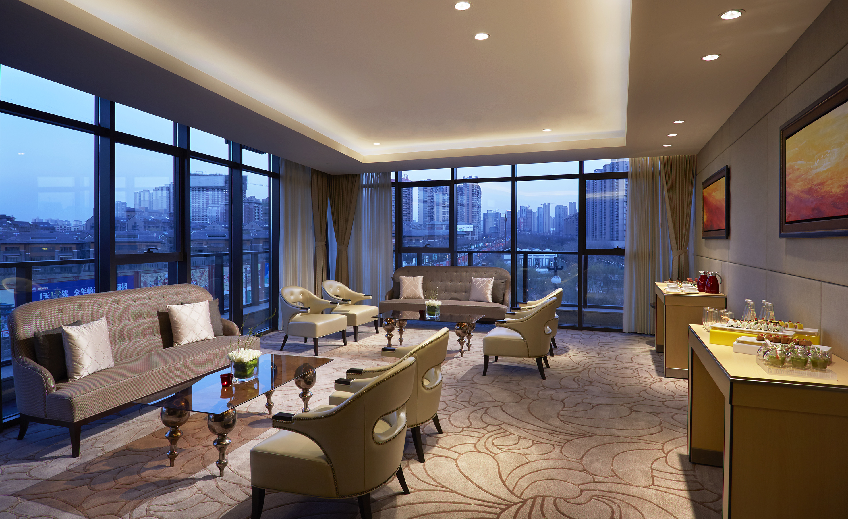 Modern hotel lounge with city view, comfortable seating, and refreshment bar.