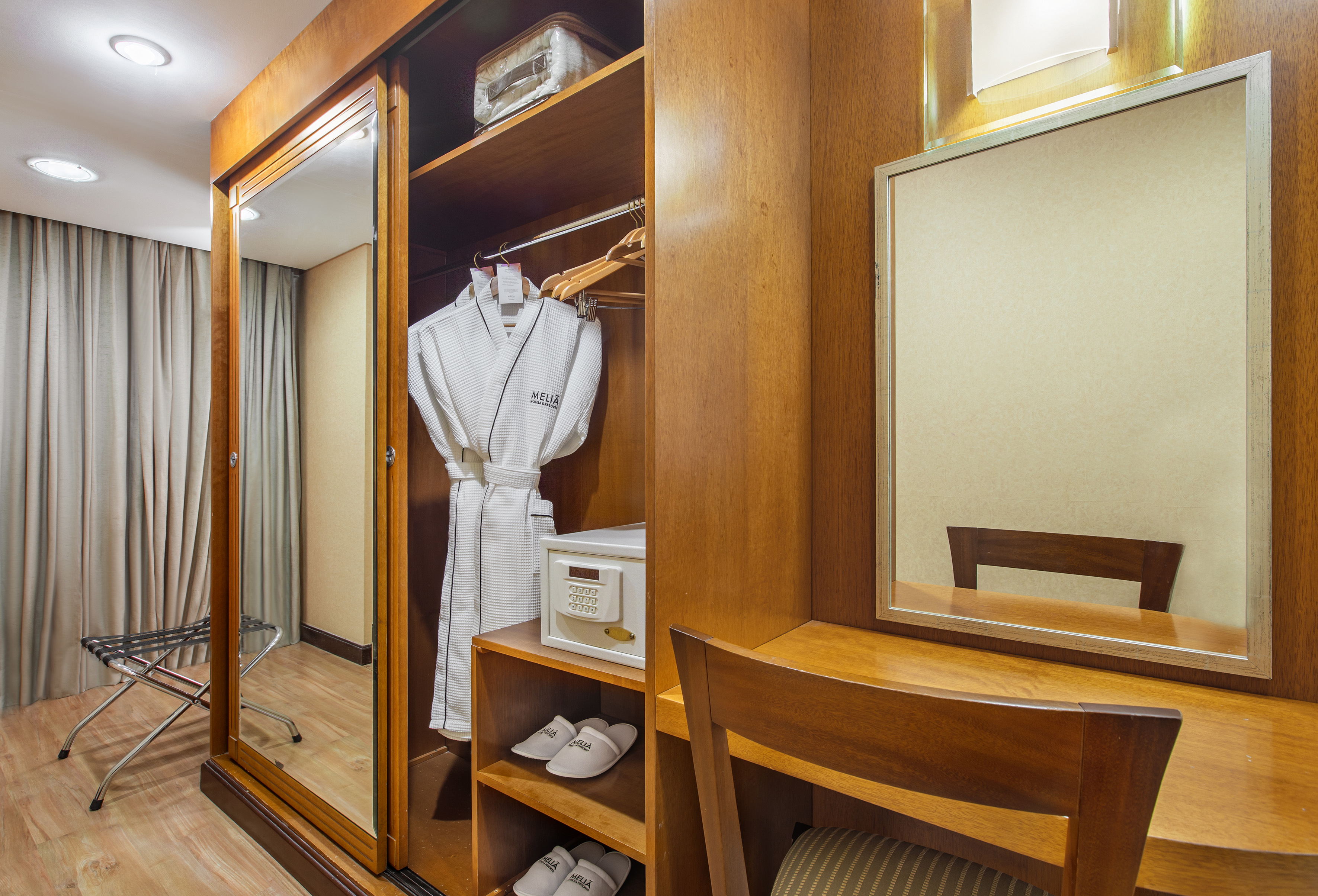 Hotel room closet with Meliá bathrobe, safe, slippers, and mirror.
