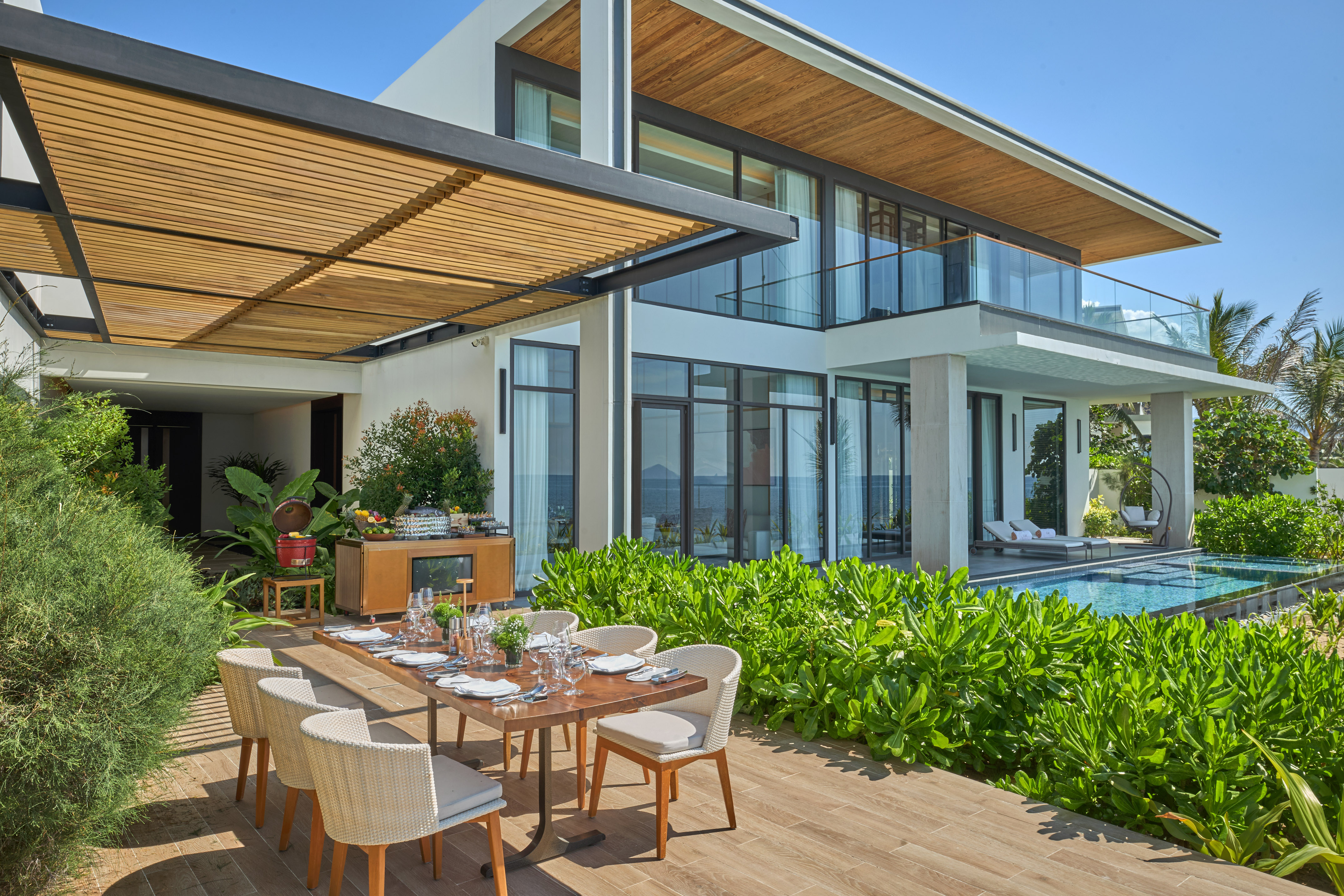 Modern luxury villa with outdoor dining patio, private pool, and ocean view.